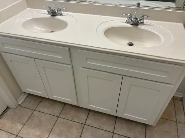 Dual vanity with integrated sinks, chrome fixtures, white shaker-style cabinetry, and tile flooring