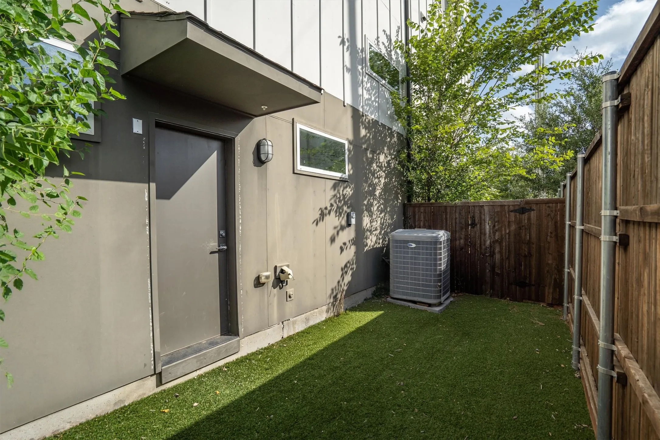 Enclosed outdoor space featuring artificial turf, a wood fence, and an exterior door with an awning