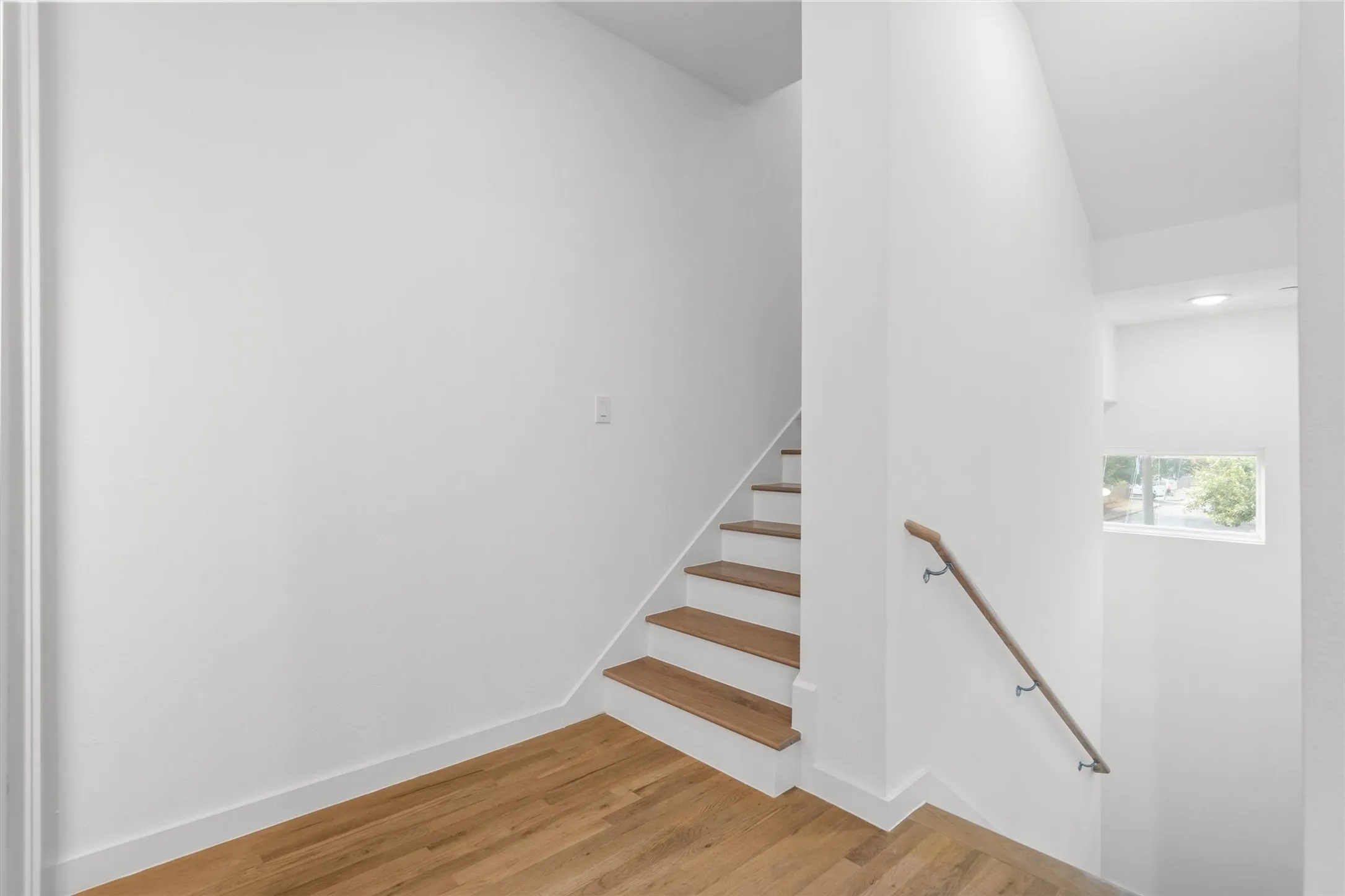 Wood-finish flooring, staircase with wood treads, white risers, and a wood handrail