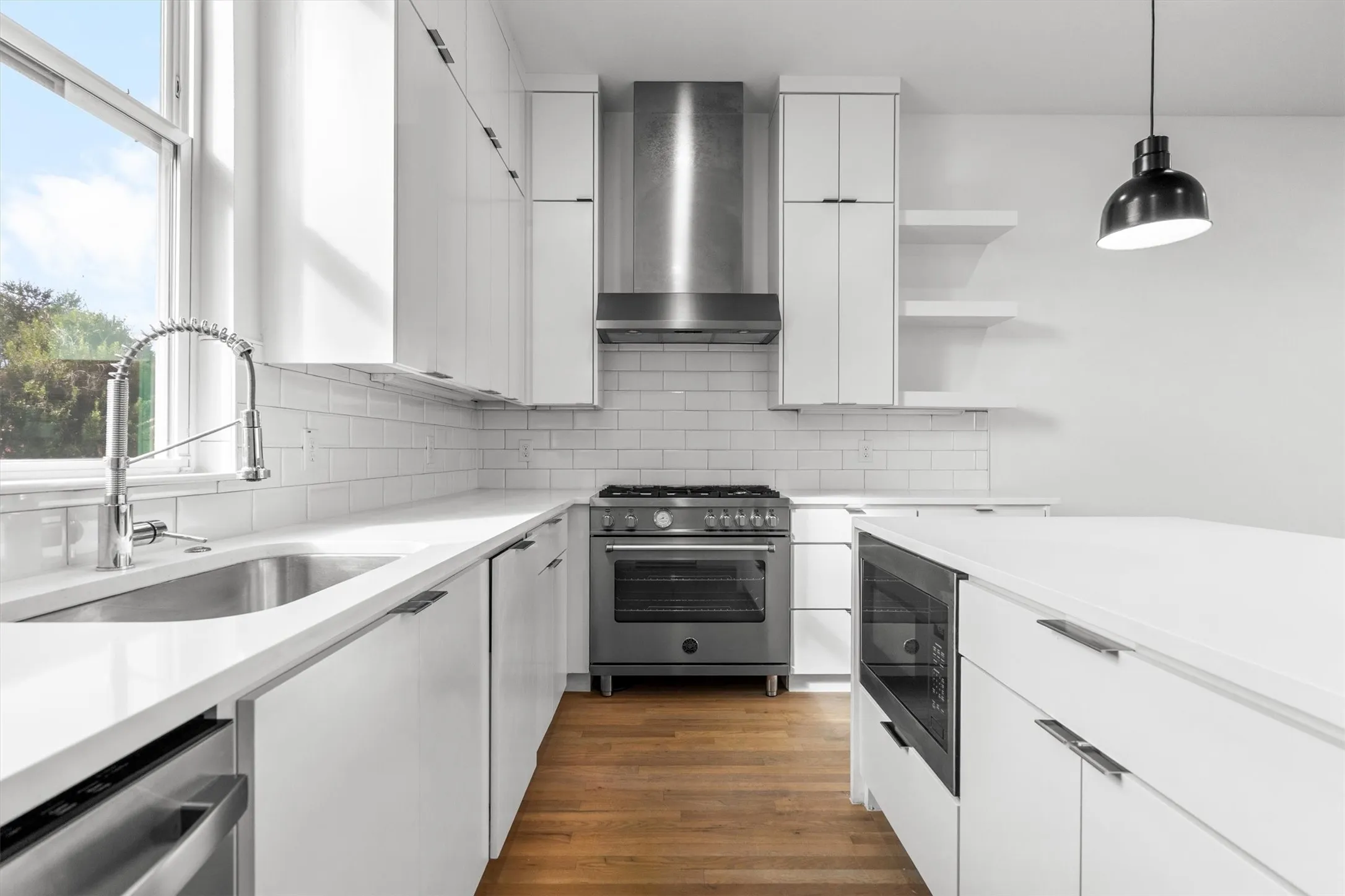 White cabinetry with sleek hardware, stainless steel appliances, light-toned countertops, white subway tile backsplash, and wood-finish flooring