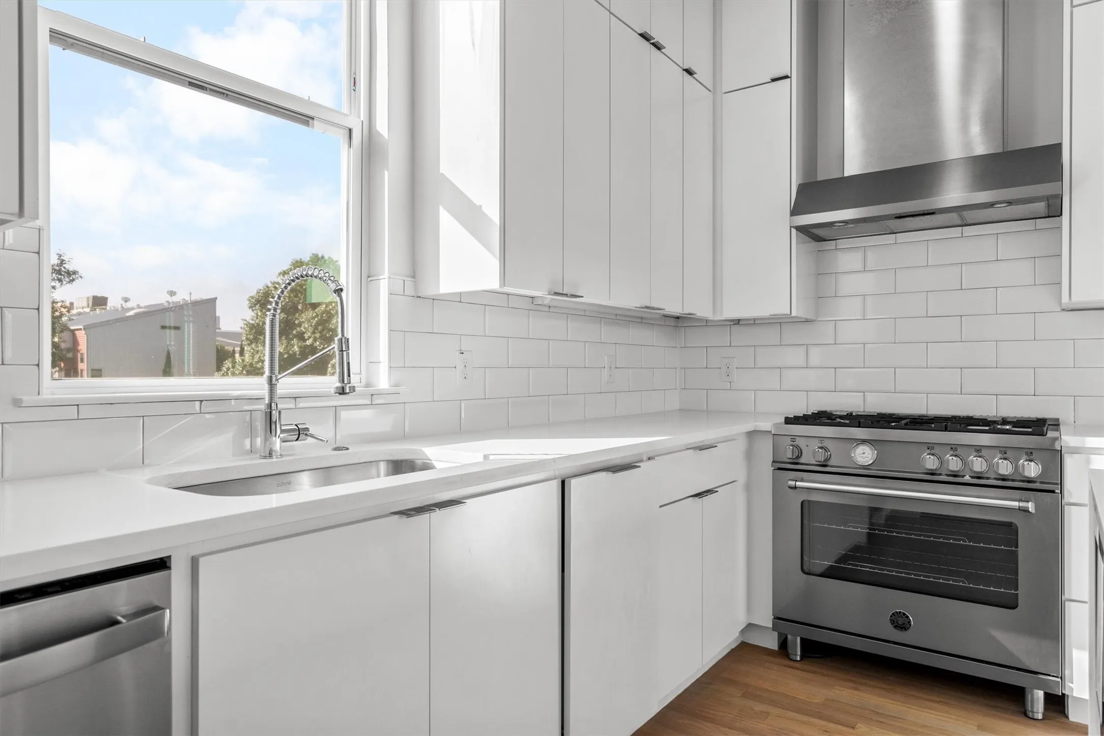 Modern kitchen featuring white cabinetry, light-toned countertops, subway tile backsplash, stainless steel range, and wood-finish flooring