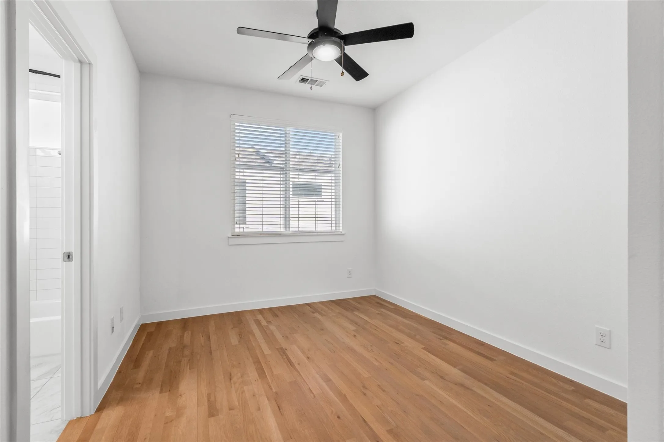 Wood-finish flooring, ceiling fan, window with blinds, and white walls