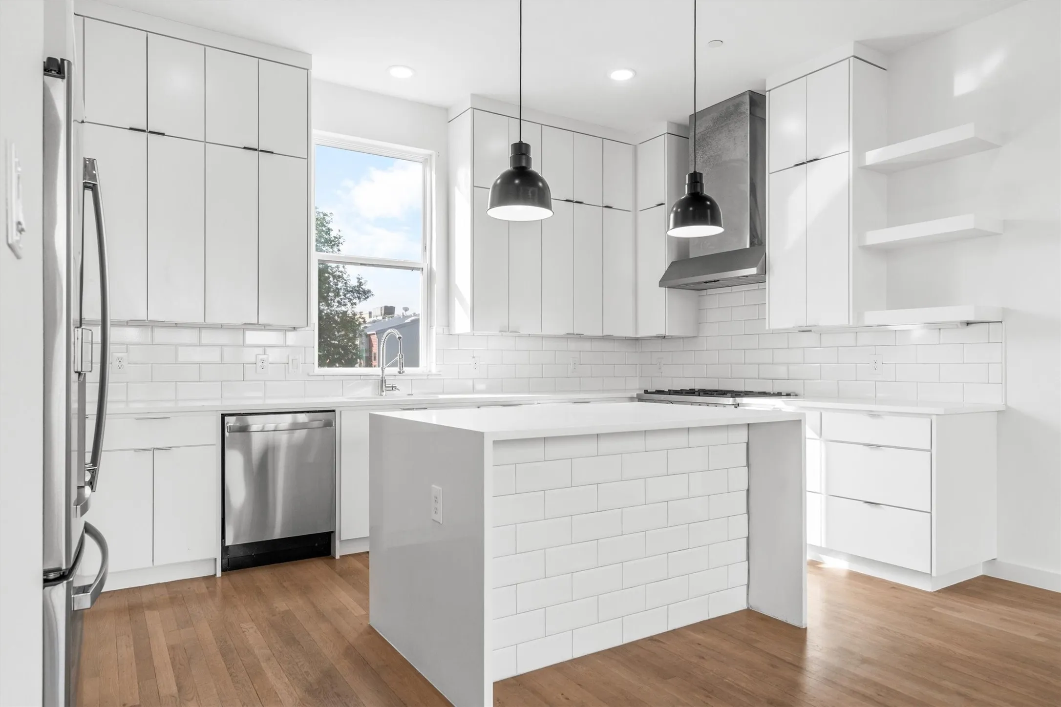 Modern kitchen featuring white flat-panel cabinetry, a central island with a white subway tile facade, stainless steel appliances, and wood-finish flooring