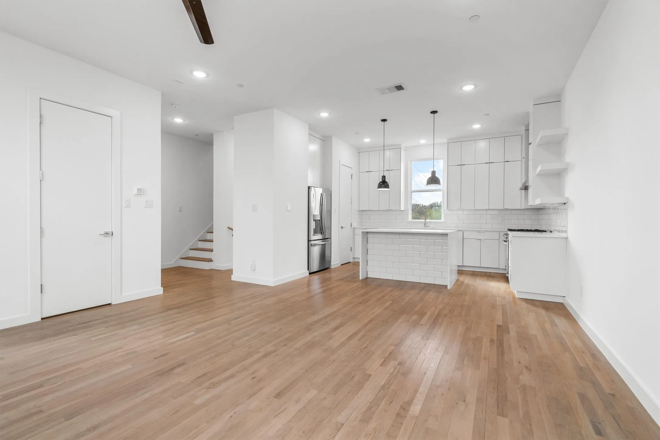 Open-concept living area featuring wood-finish flooring, recessed lighting, and a kitchen with white cabinetry, a subway tile backsplash, and stainless steel appliances