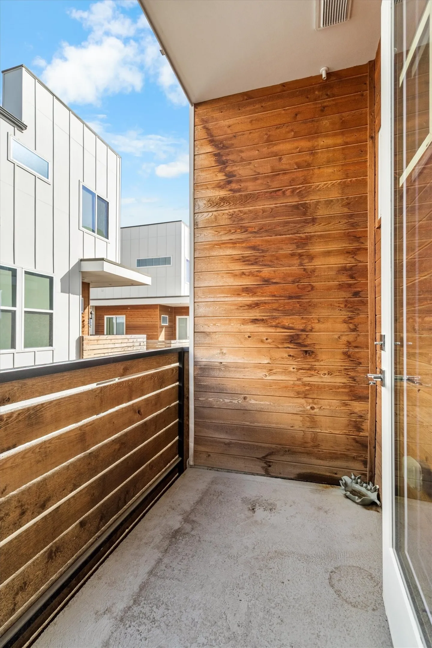 Balcony with concrete flooring and wood paneling, featuring a slatted wood railing