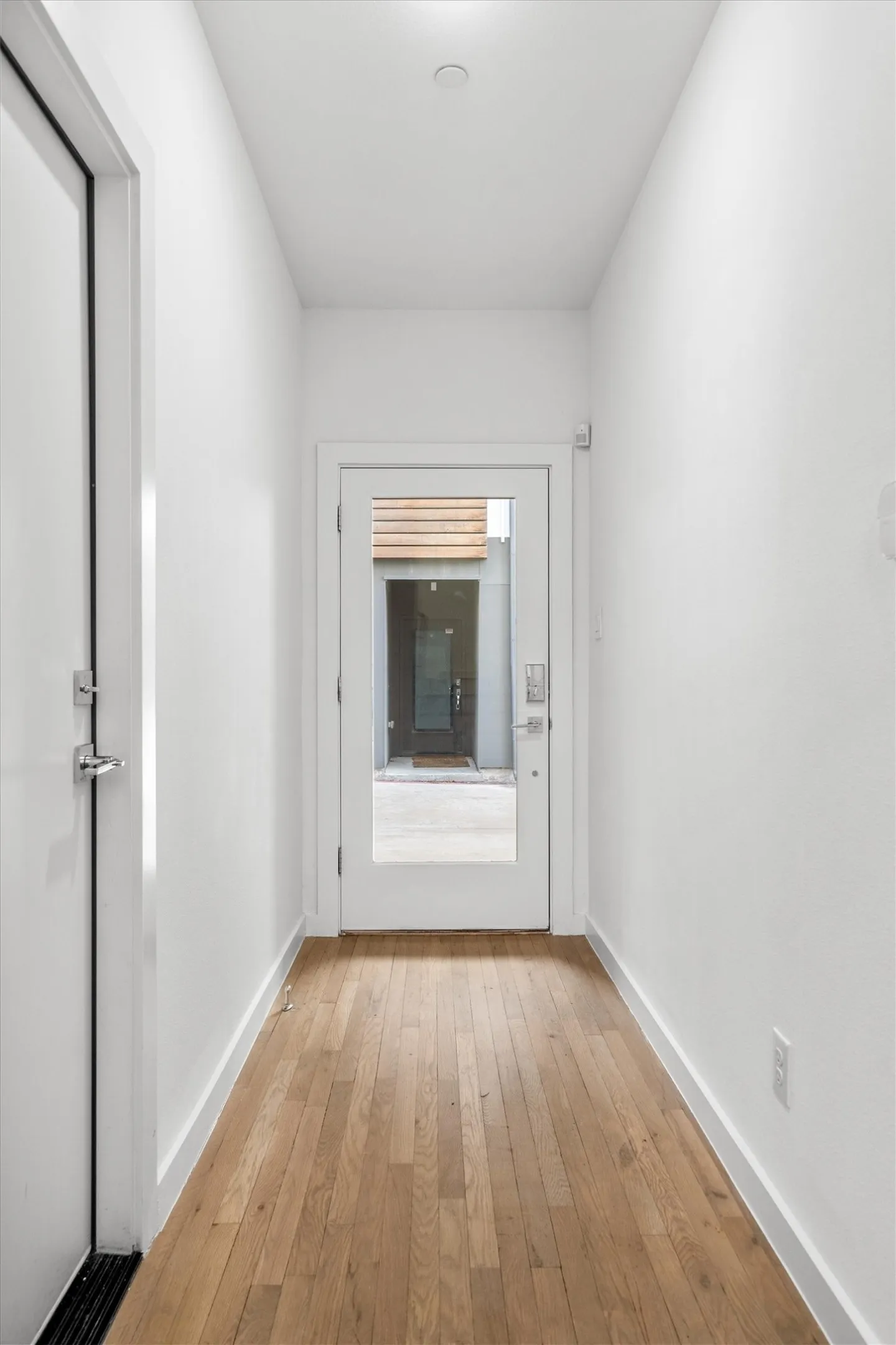 Wood-finish flooring with white baseboards, recessed ceiling lighting, and a full-light entry door