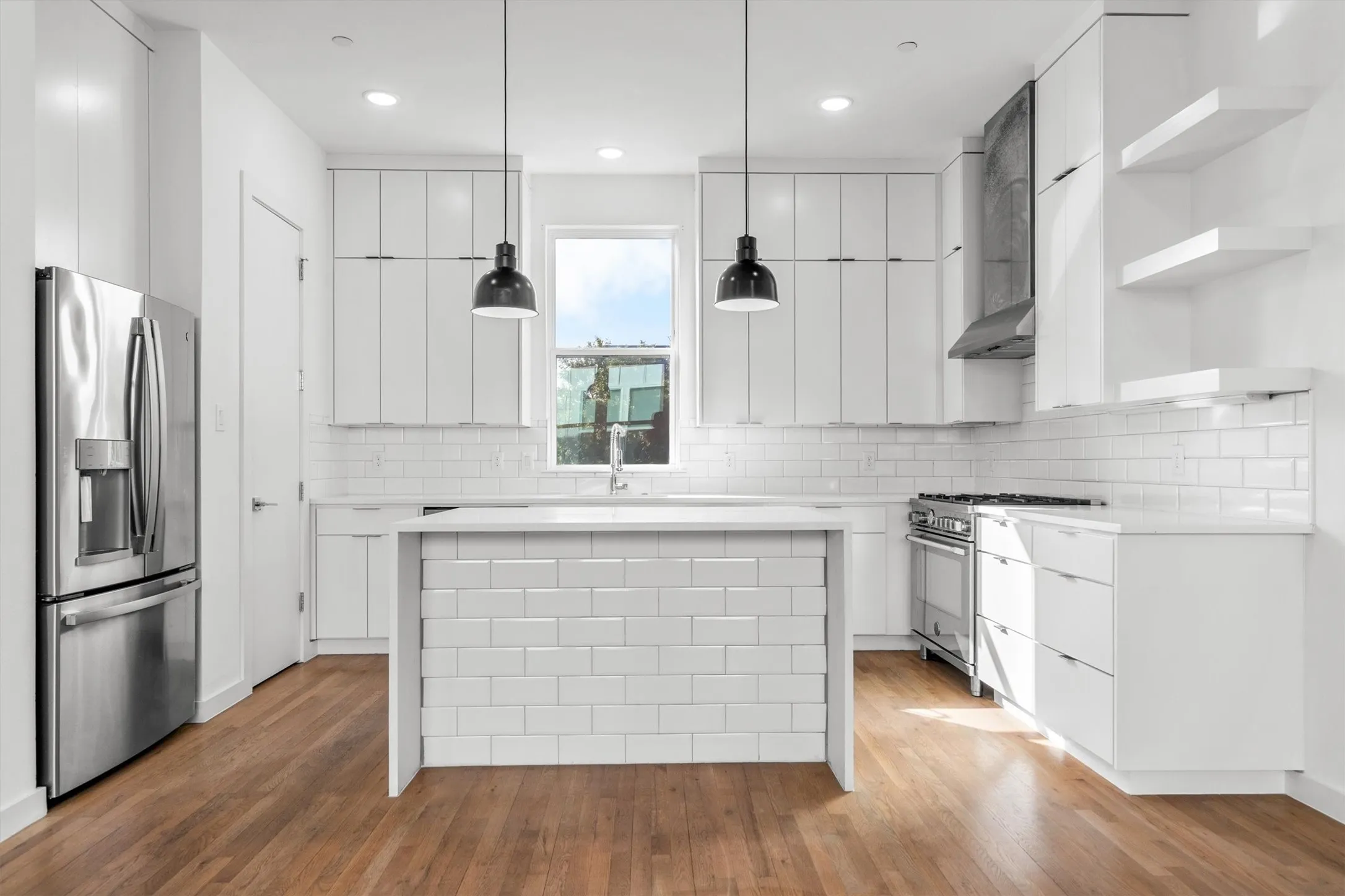 Bright kitchen featuring wood-finish flooring, white cabinetry, a subway tile backsplash, and stainless steel appliances