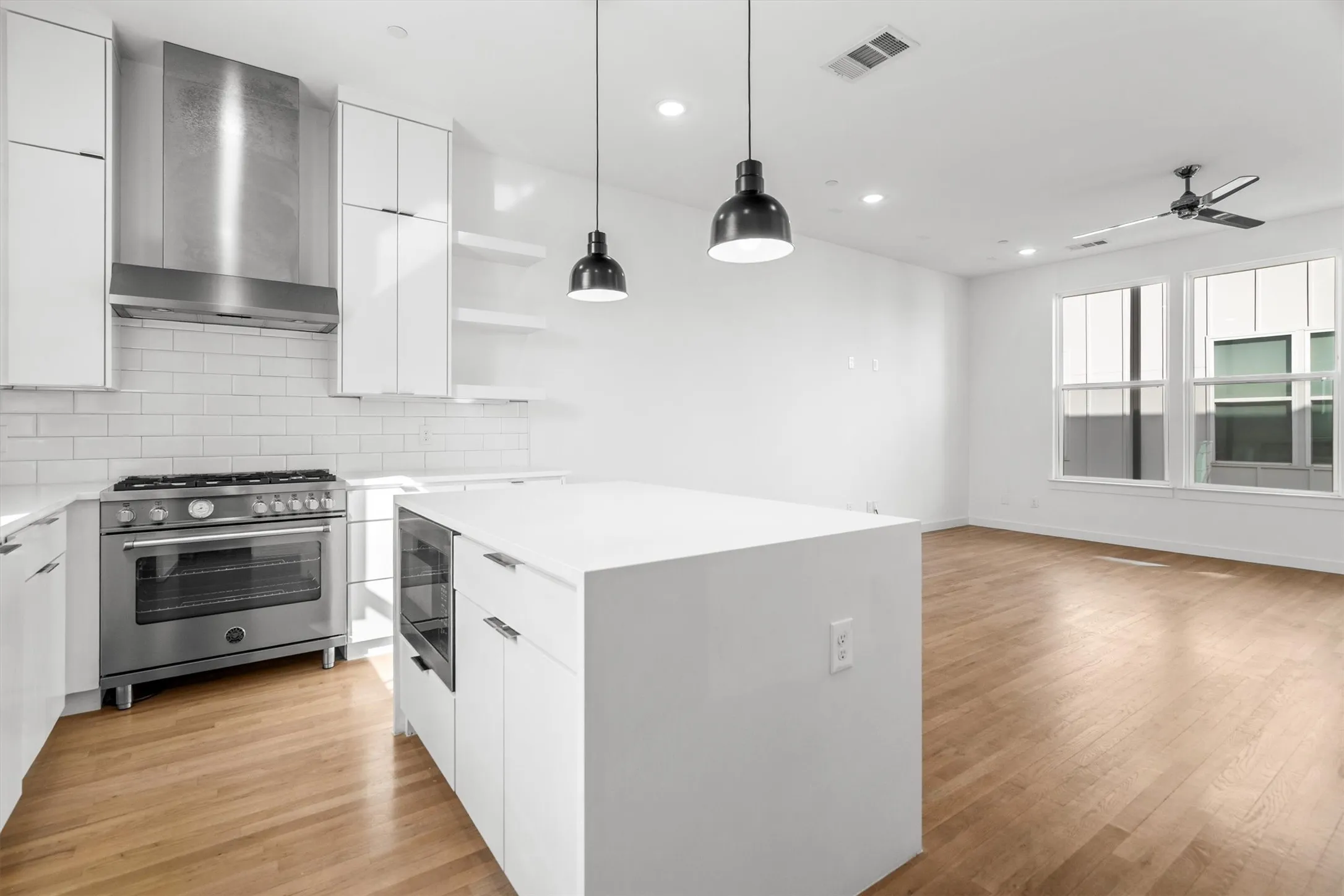 Modern kitchen featuring white cabinetry, subway tile backsplash, stainless steel range with hood, and a central island with integrated oven