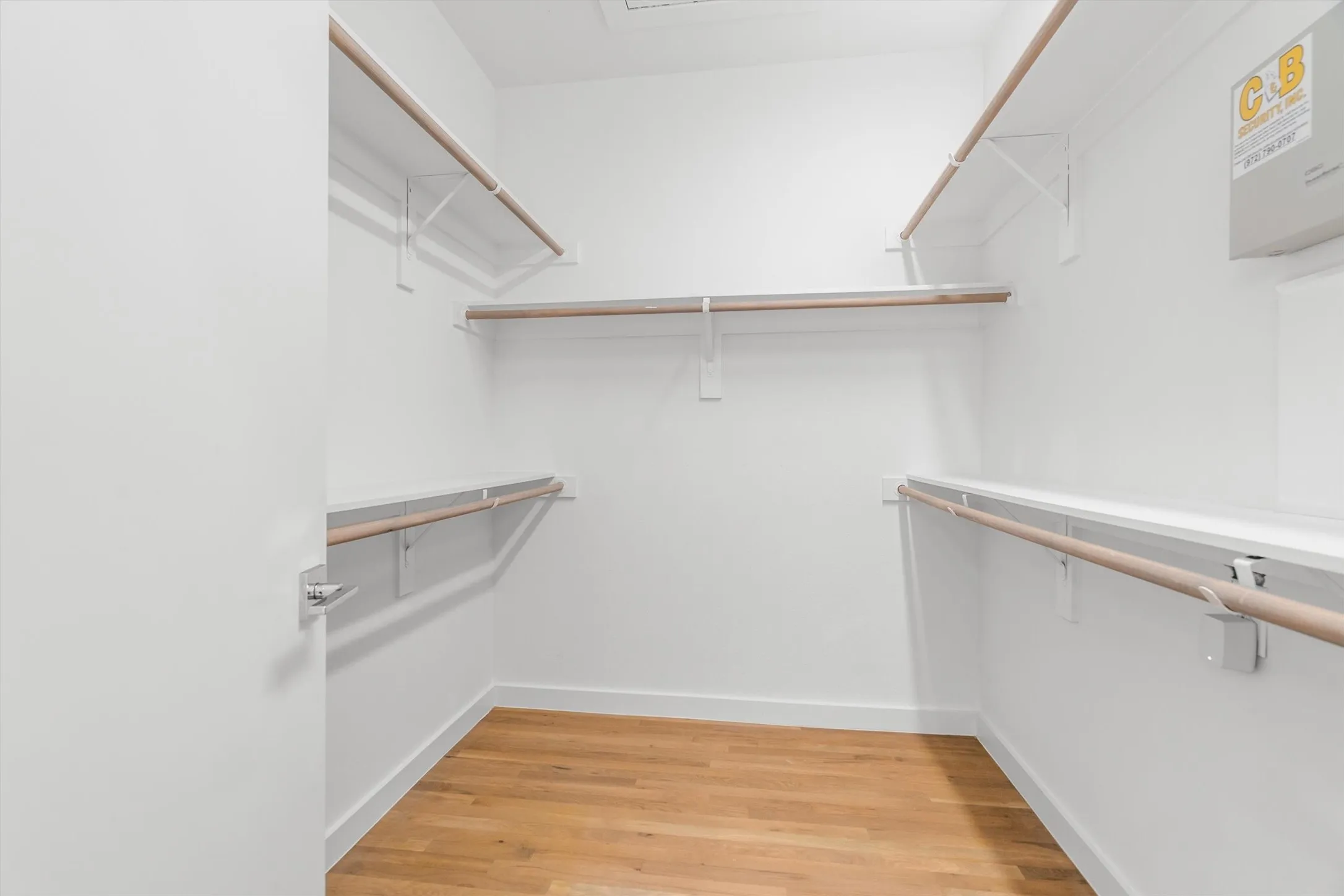 Walk-in closet featuring wood-finish flooring, white walls, and built-in shelving with hanging rods