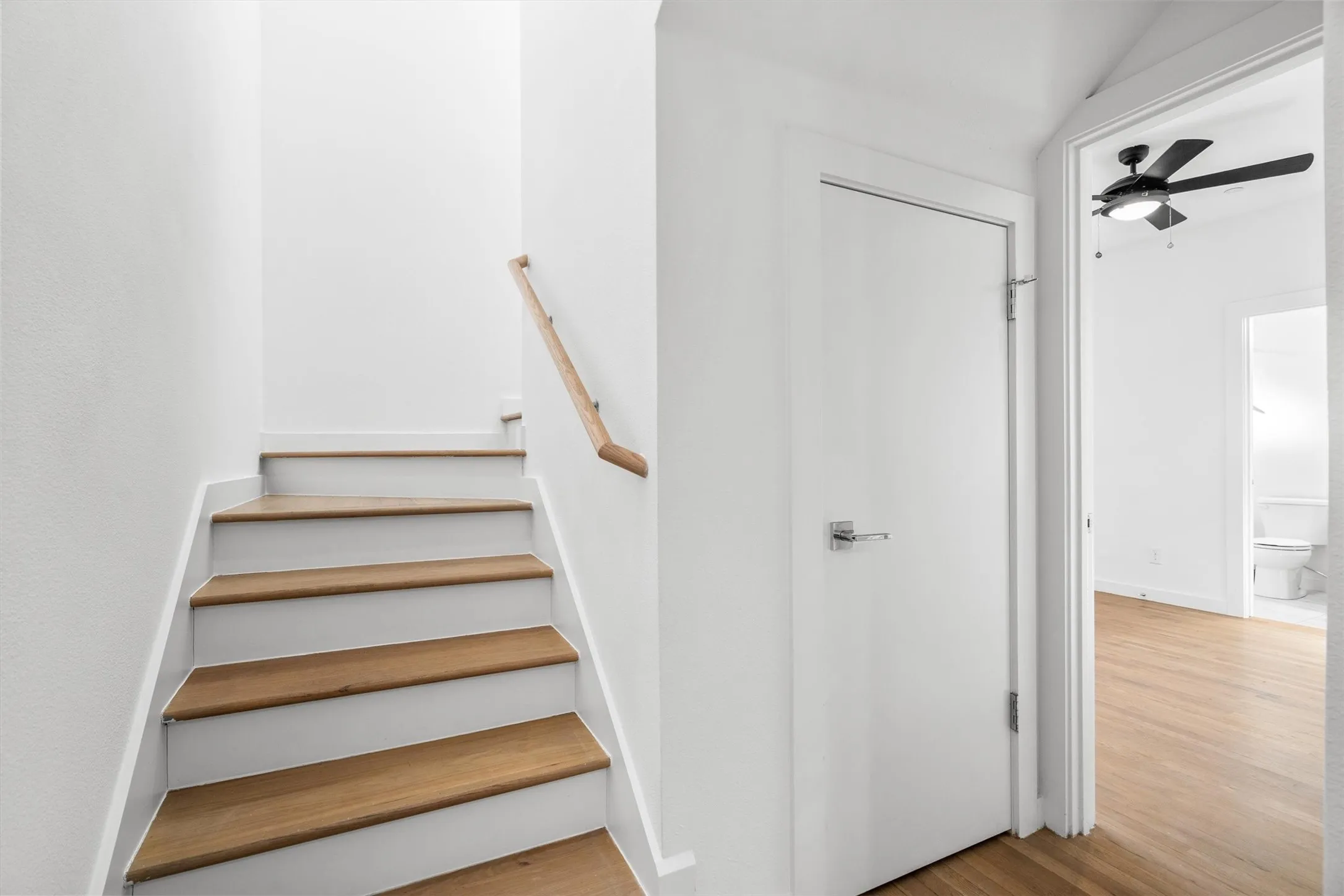 Staircase with wood-finish treads and white risers, featuring a light wood-finish handrail