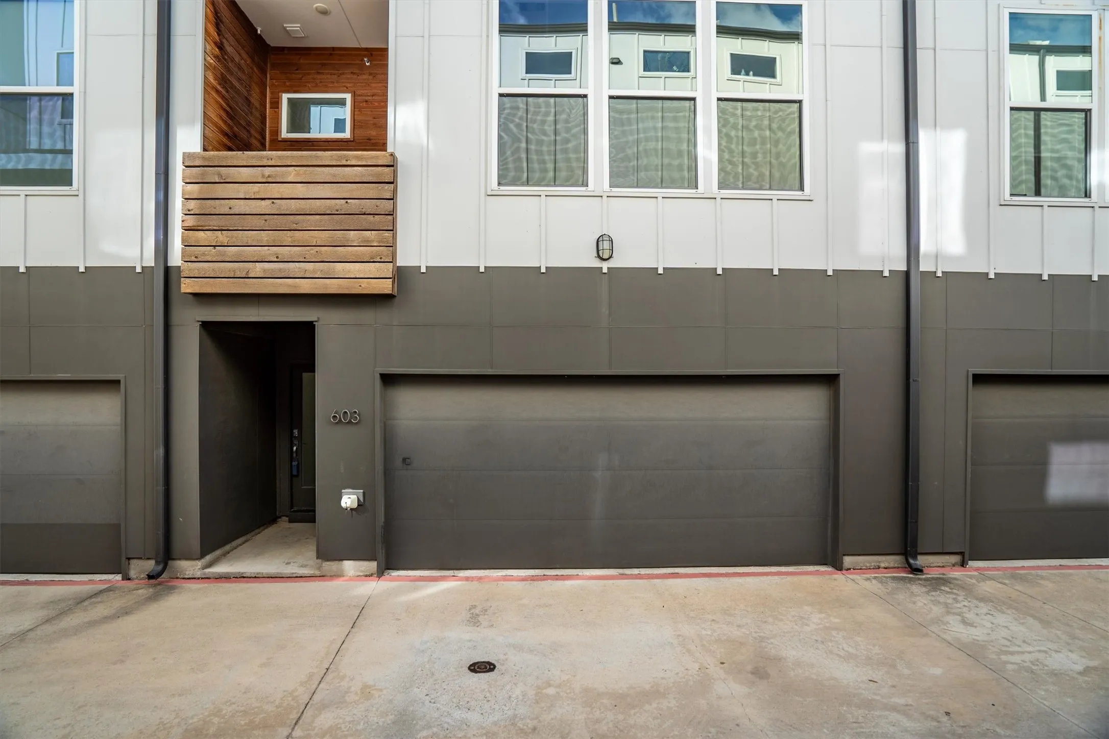 Modern exterior featuring a prominent two-car garage, upper-level balcony with wood slat railing, and multi-pane windows