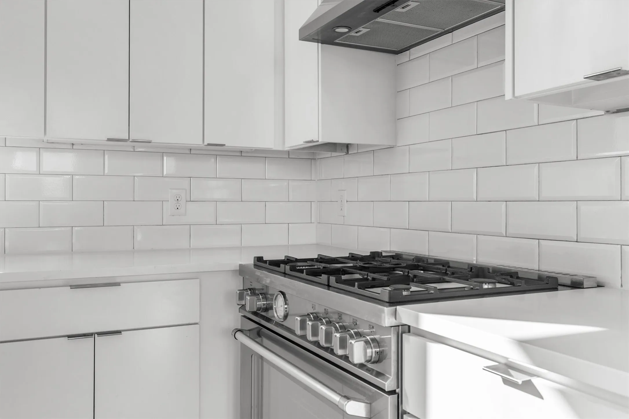 Stainless steel range, coordinating range hood, white subway tile backsplash, white countertops, and white upper and lower cabinetry