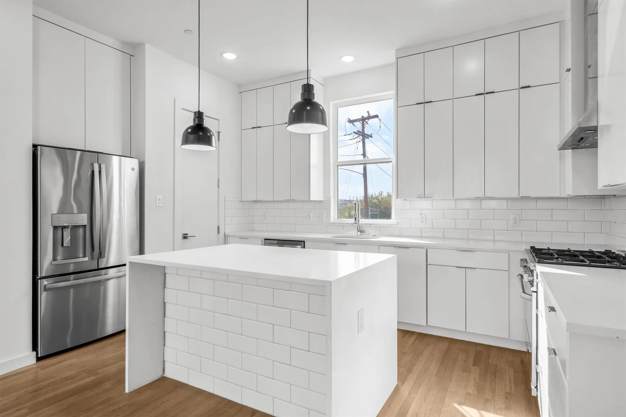 Contemporary kitchen with white cabinetry, stainless steel appliances, wood-finish flooring, white subway tile backsplash, and a central island with a solid surface countertop