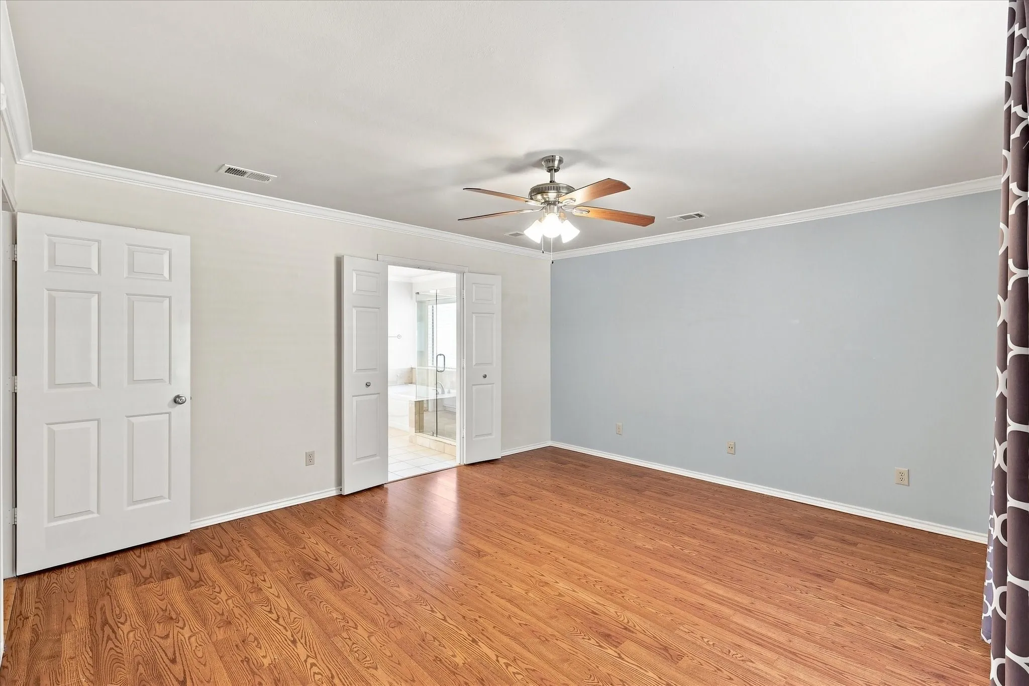 Wood-finish flooring, crown molding, ceiling fan with light fixture, and bifold doors opening to an adjoining room