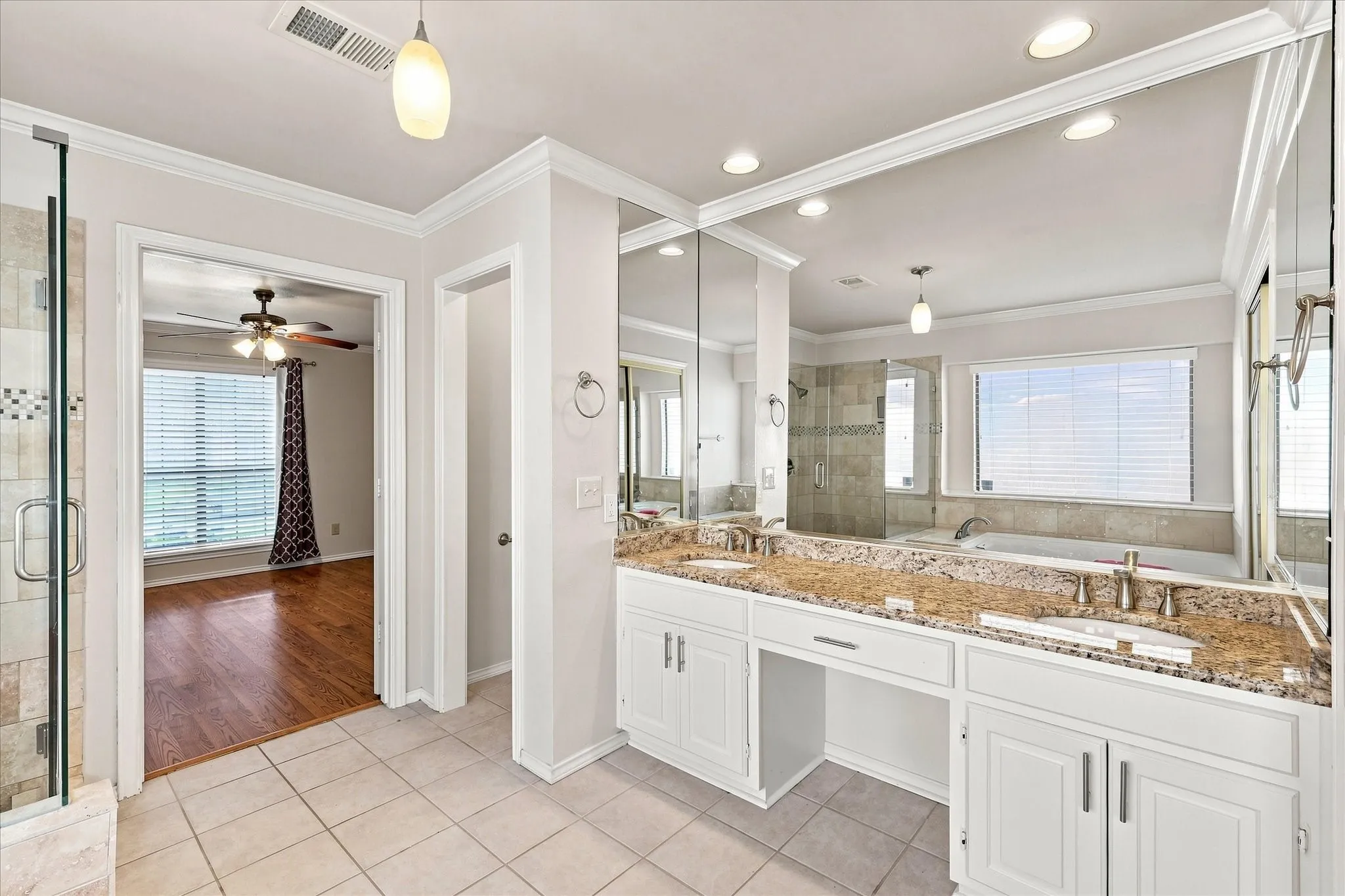 Double vanity with stone countertop, integrated sinks, large mirrored wall, and recessed lighting
