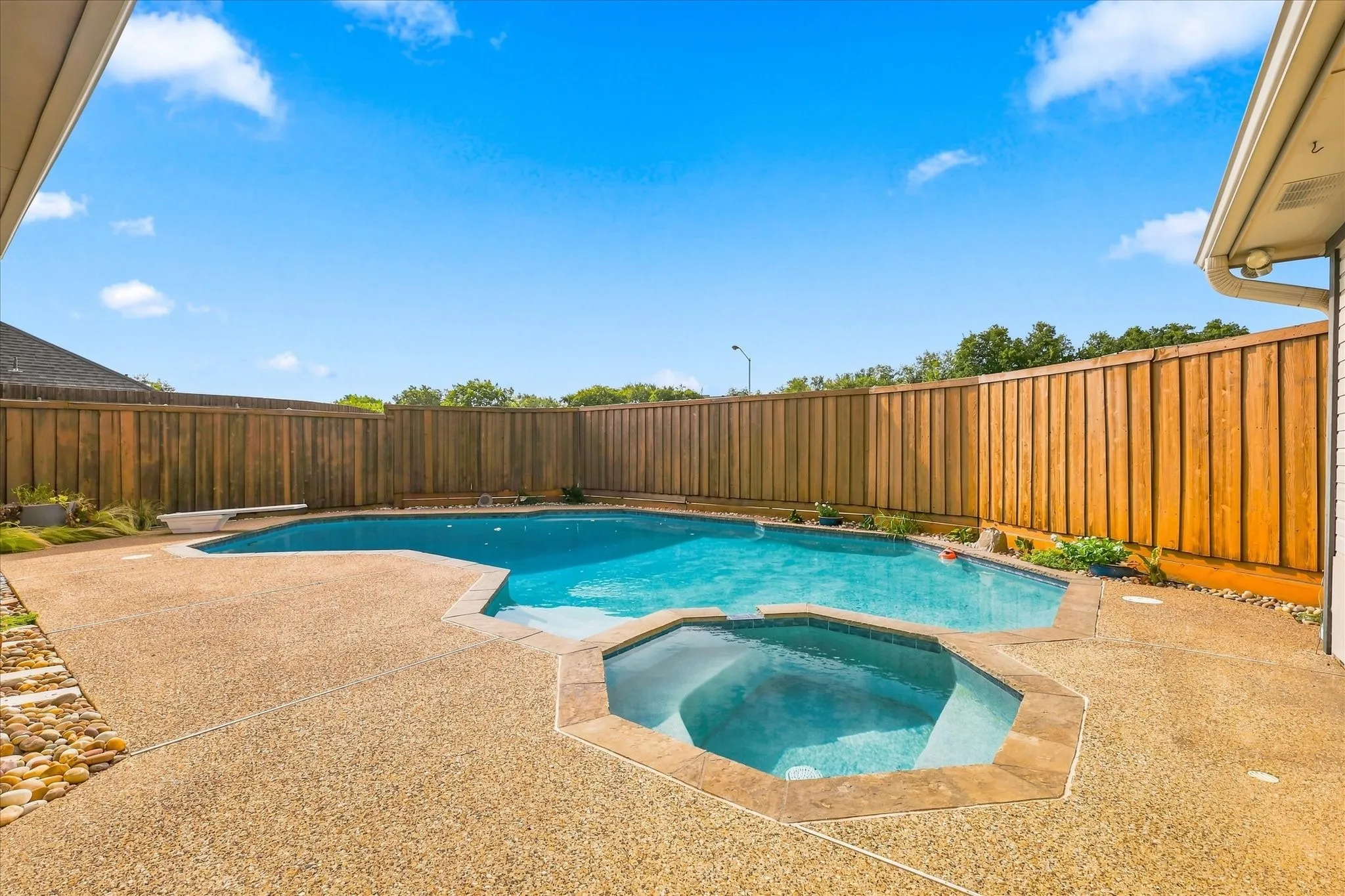Backyard featuring a freeform swimming pool, integrated spa, exposed aggregate concrete deck, and a wood privacy fence