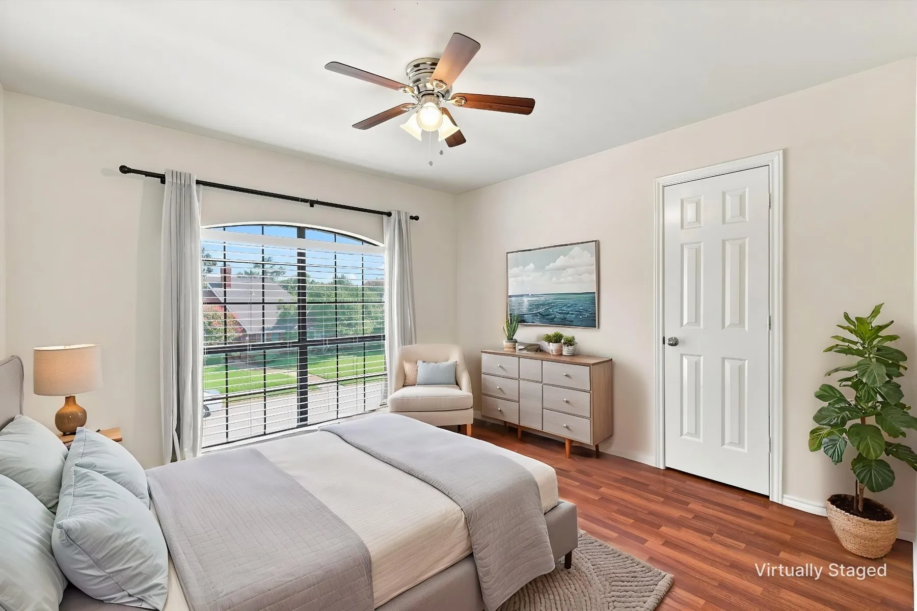 Arched window with blinds, ceiling fan with light fixture, wood-finish flooring, white paneled door, and neutral wall tones