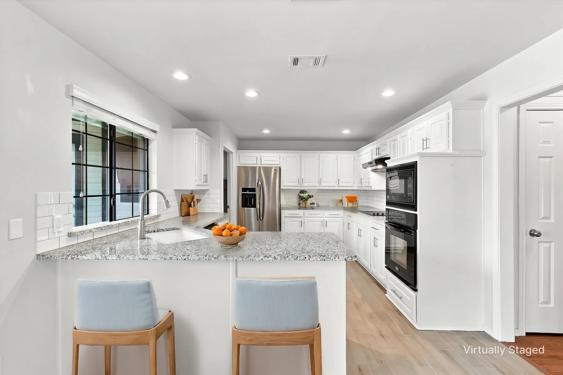 White cabinetry, granite countertops, subway tile backsplash, stainless steel appliances, and wood-finish flooring