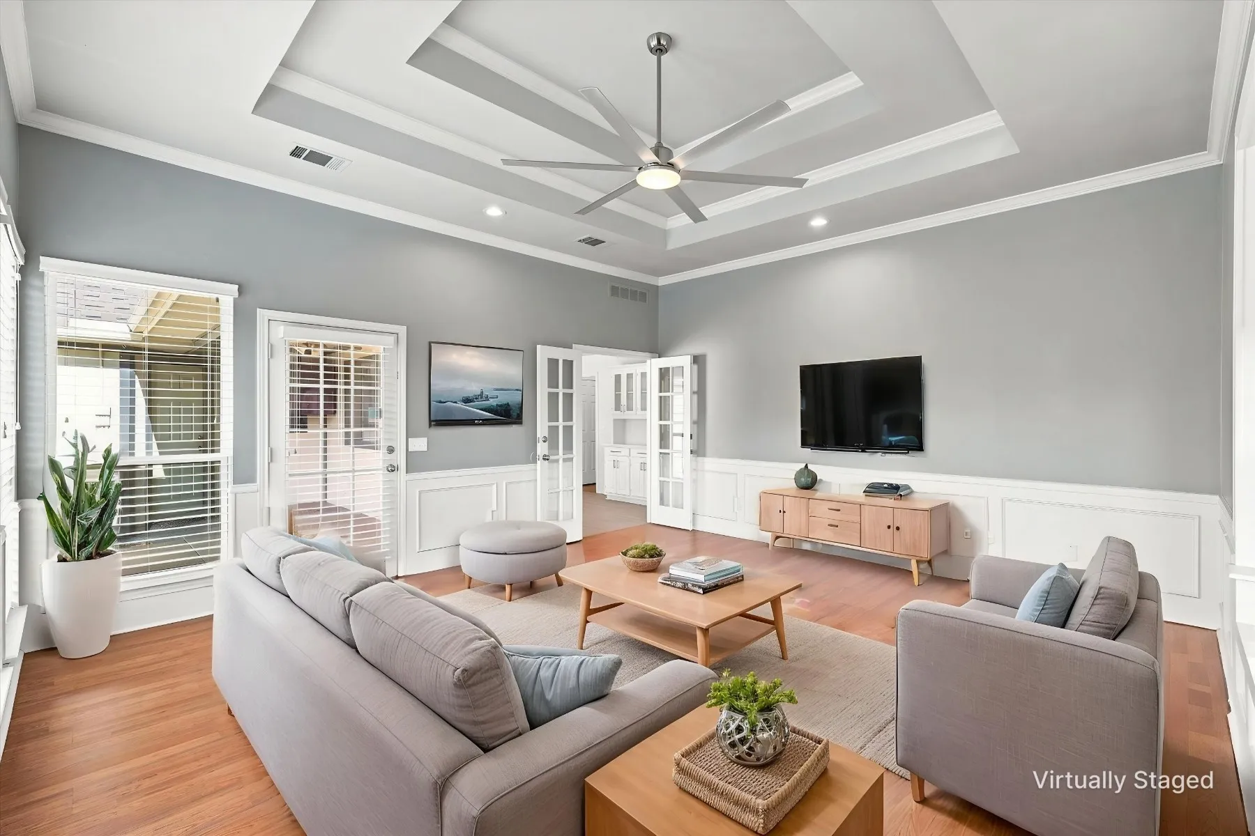 Tray ceiling with crown molding, ceiling fan, wood-finish flooring, wainscoting, and French doors