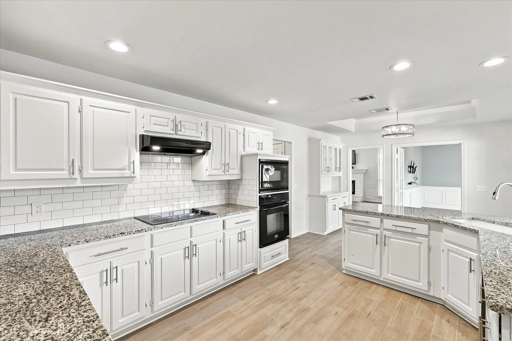Kitchen with white cabinetry, granite-style countertops, subway tile backsplash, wood-finish flooring, and recessed lighting