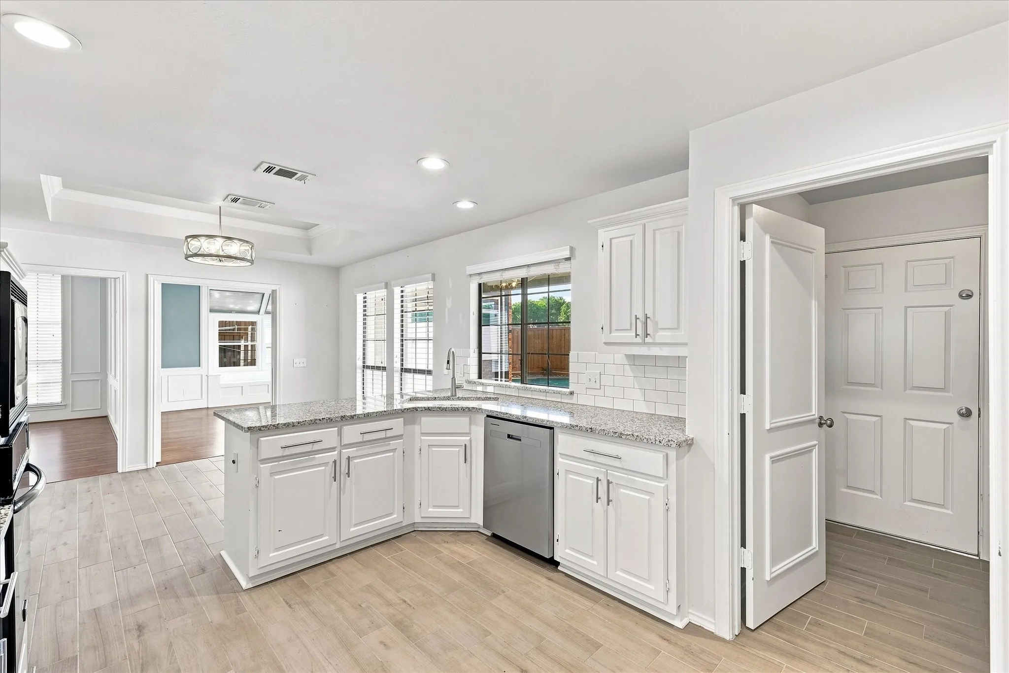 White shaker cabinetry, wood-finish flooring, stainless steel appliances, granite countertops, and subway tile backsplash
