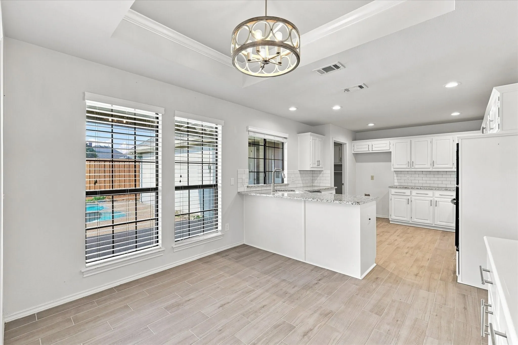 Recessed lighting, wood-finish tile flooring, tray ceiling, kitchen island with stone countertop, and white cabinetry