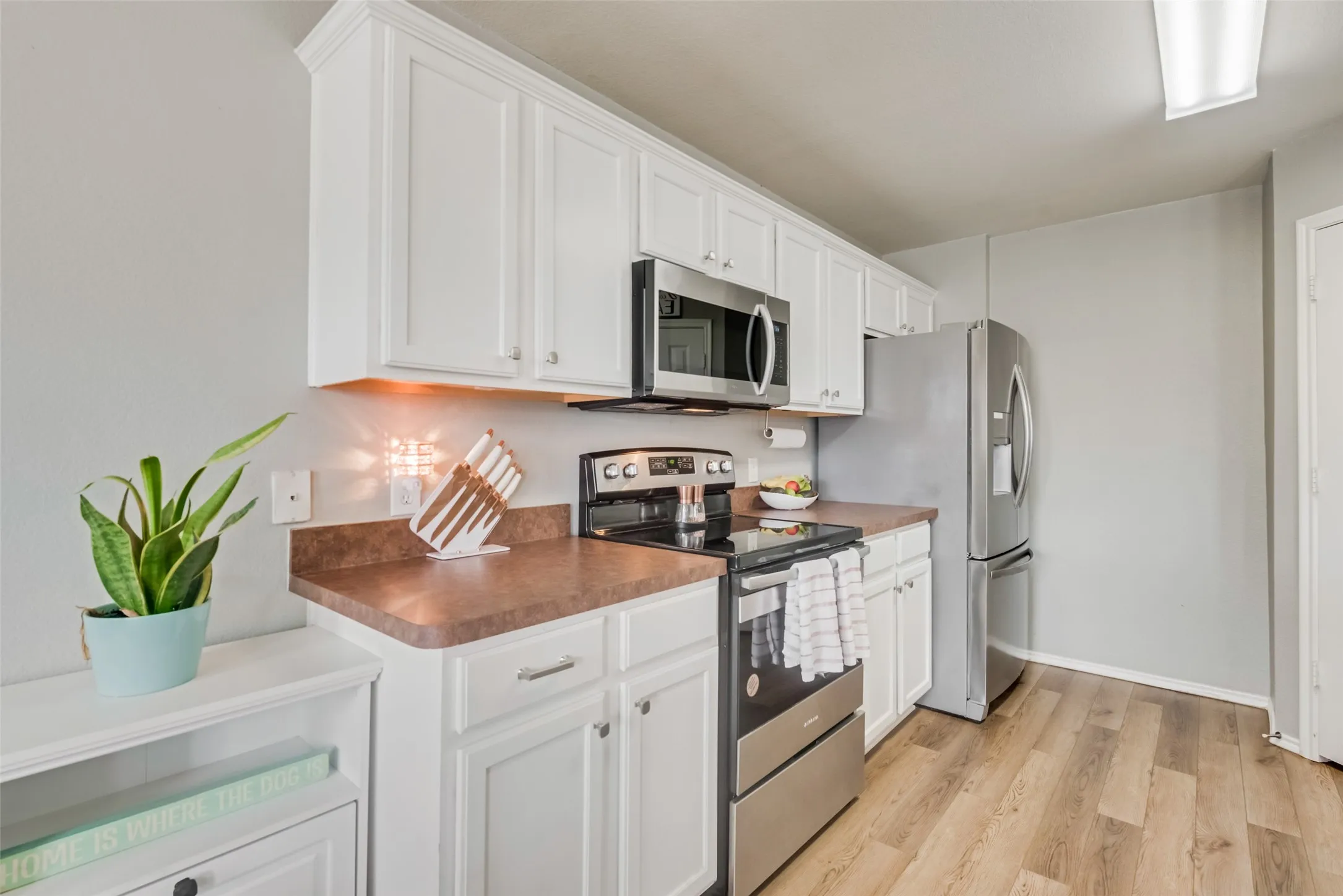 White cabinetry with crown molding, stainless steel appliances, wood-finish flooring, and a built-in microwave