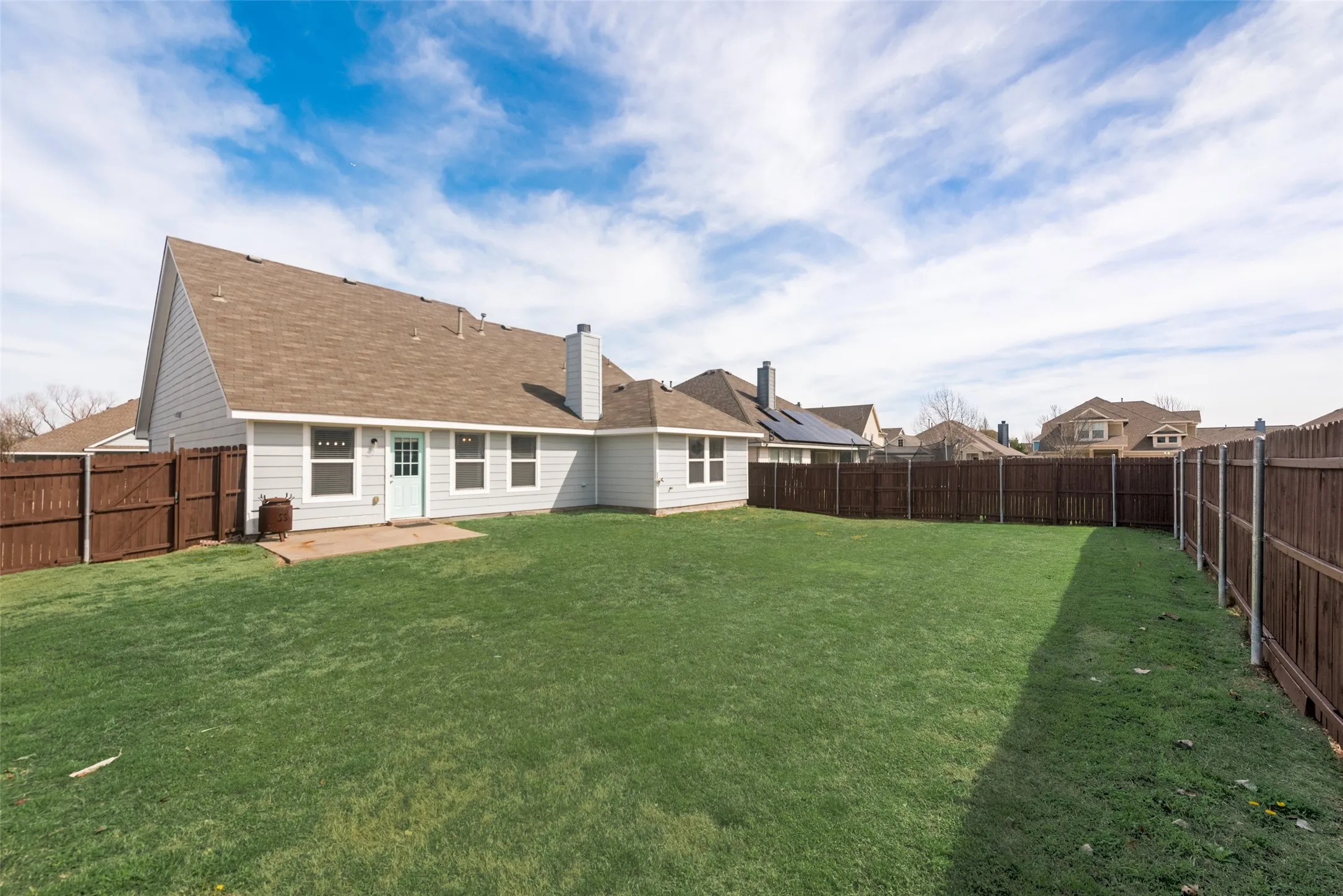 Expansive backyard with a green lawn, wood fence, and a concrete patio