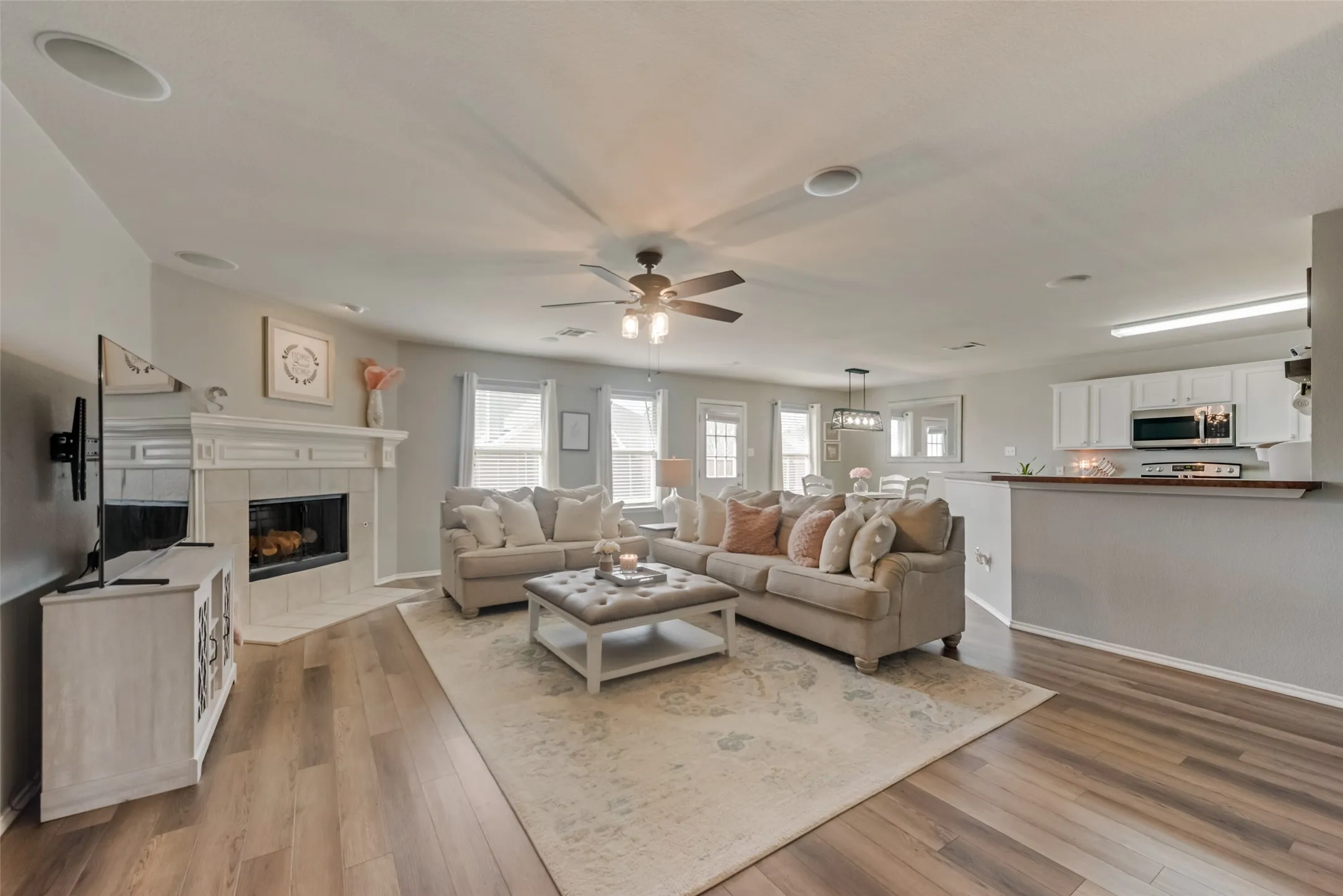 Wood-finish flooring throughout, white mantel fireplace with tile surround, ceiling-mounted speakers, and a ceiling fan with integrated lighting
