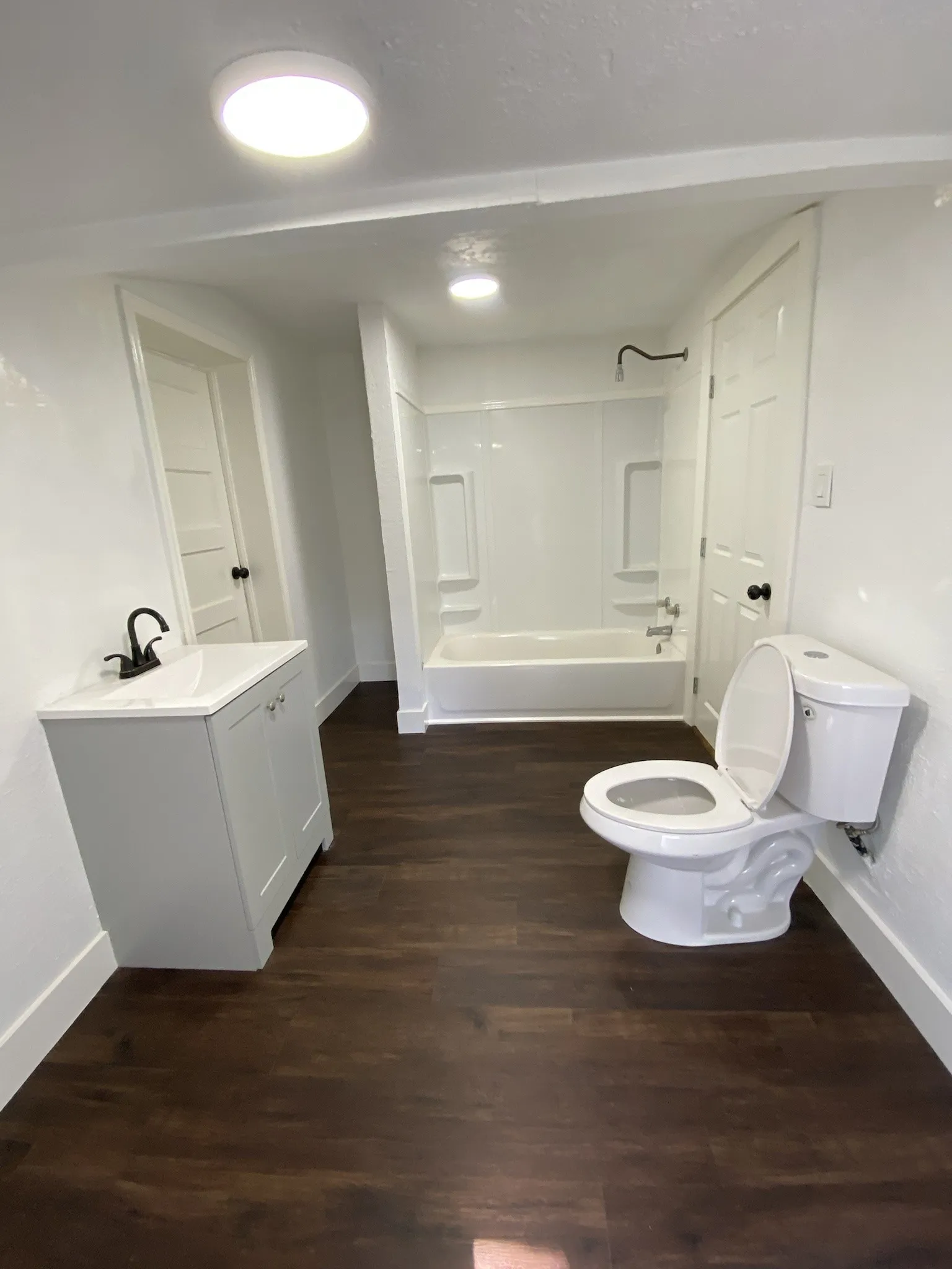 Wood-finish flooring, white walls, and a contemporary vanity with a black faucet