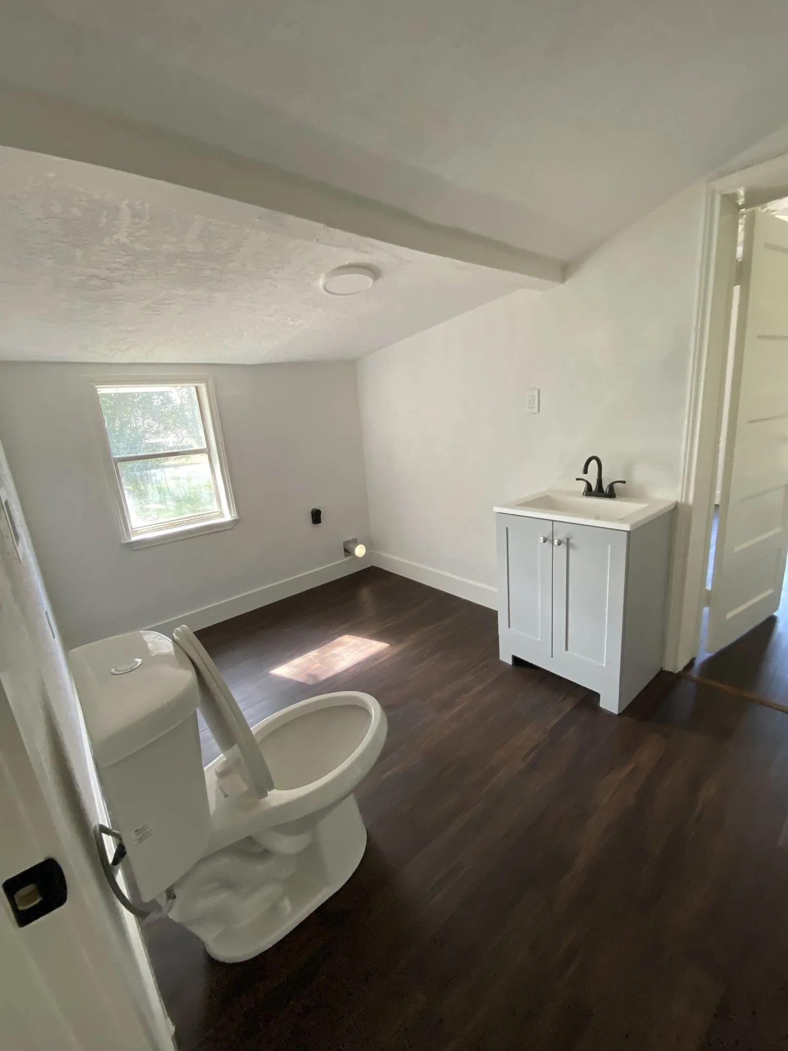Wood-finish flooring, built-in vanity cabinet with integrated sink and matte black faucet, and a window for natural light