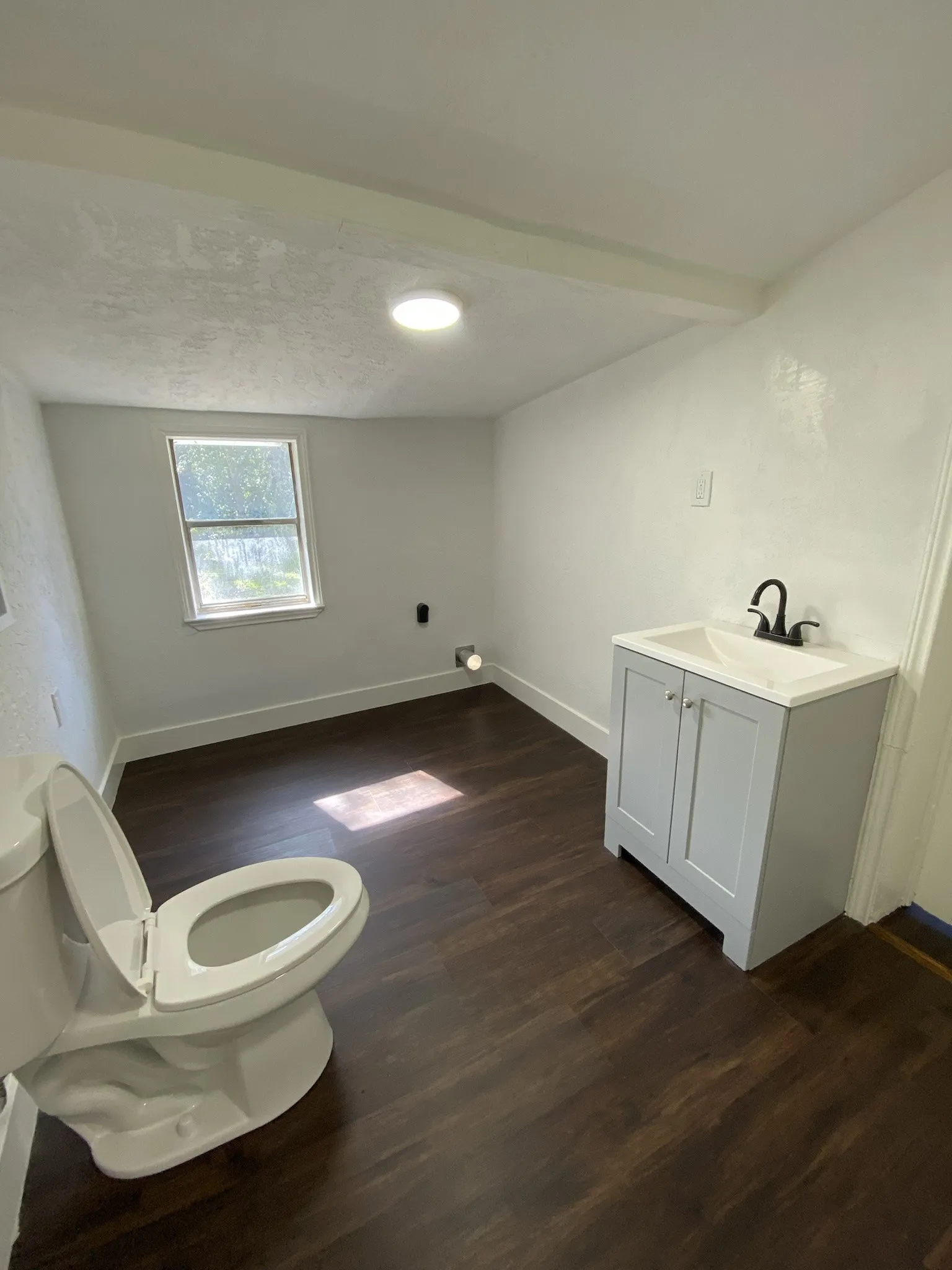 Dark wood-finish flooring with a light gray vanity, white countertop, and modern black faucet