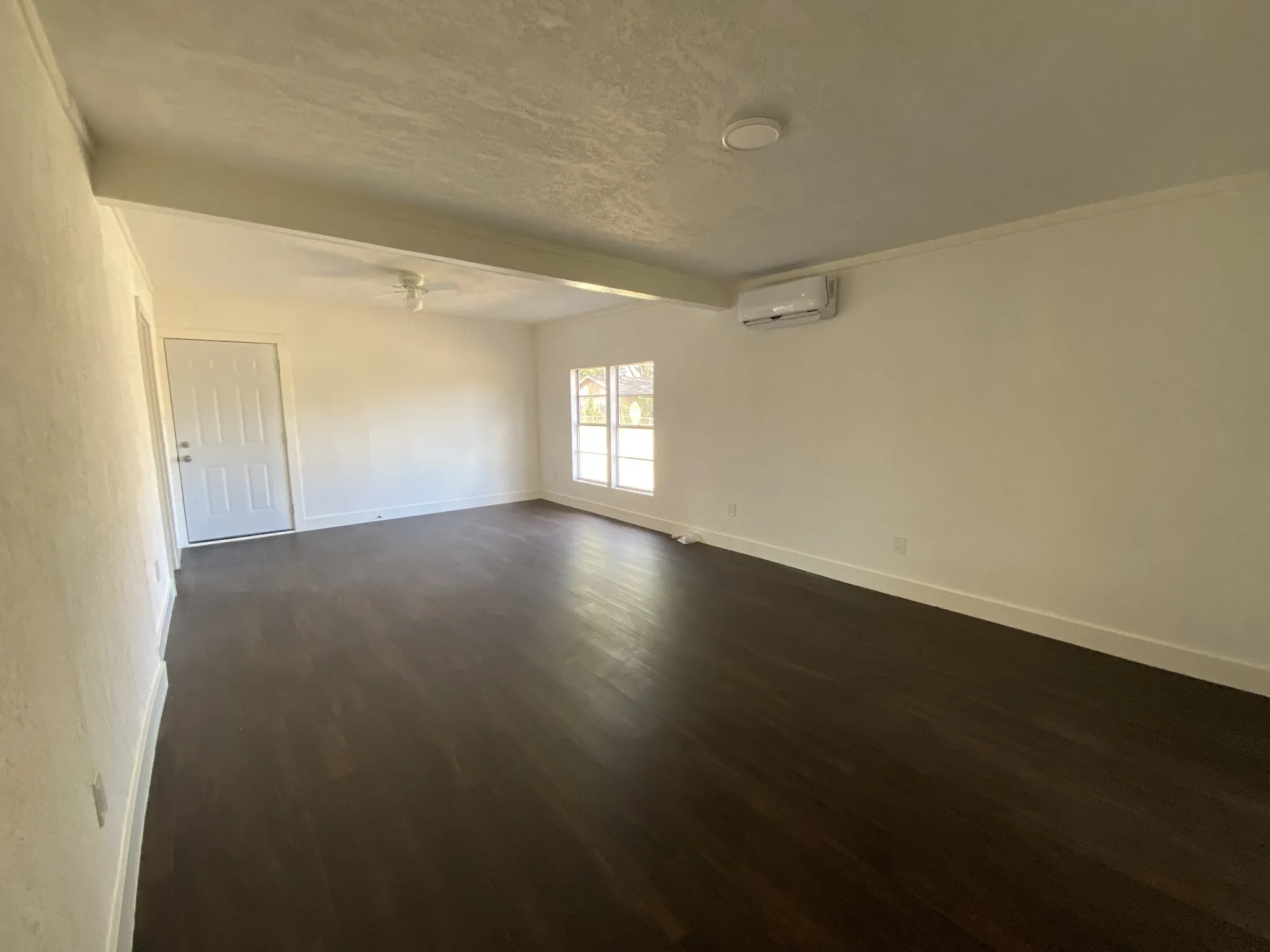 Dark wood-finish flooring, white walls, ceiling-mounted light fixture, split air conditioning unit, and multi-pane window