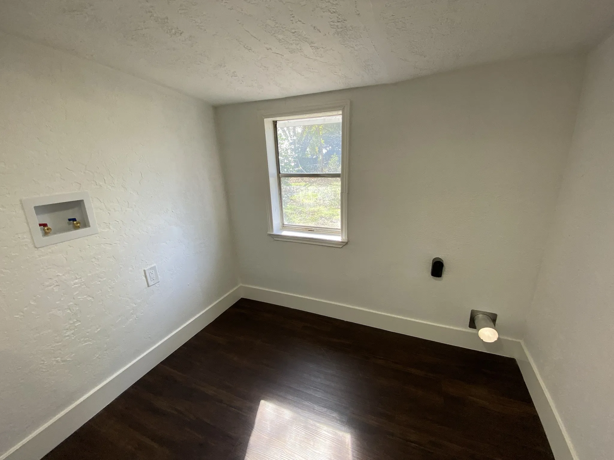 Room featuring wood-finish flooring, white walls, and a window with white trim