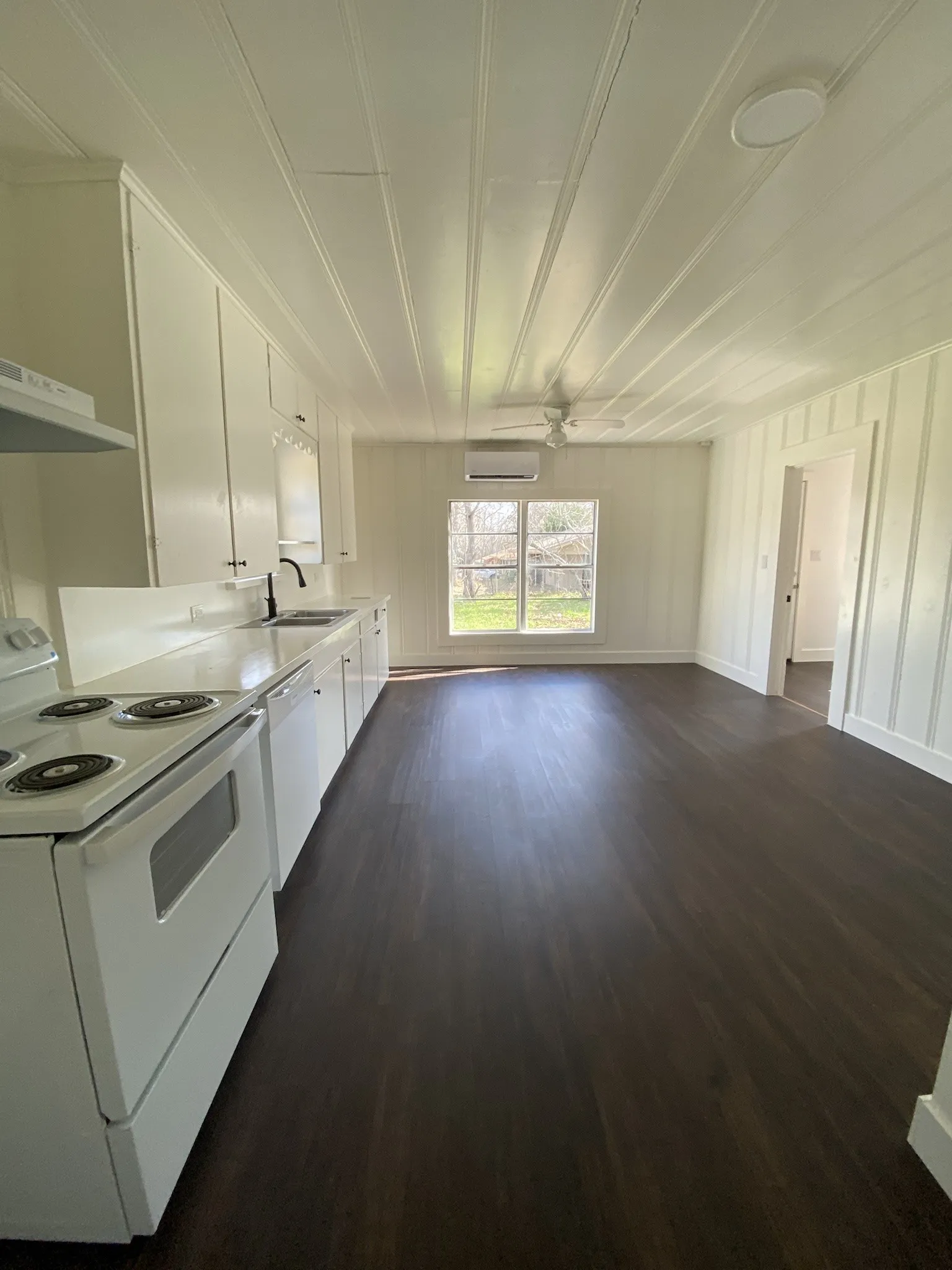 Open-concept living space with dark wood-finish flooring, white paneling, and a ceiling fan