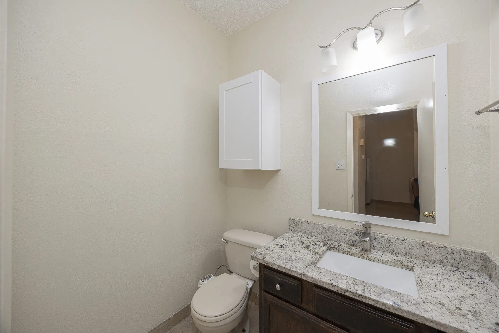 Vanity featuring a granite-finish countertop, single basin sink, and dark wood-finish cabinetry