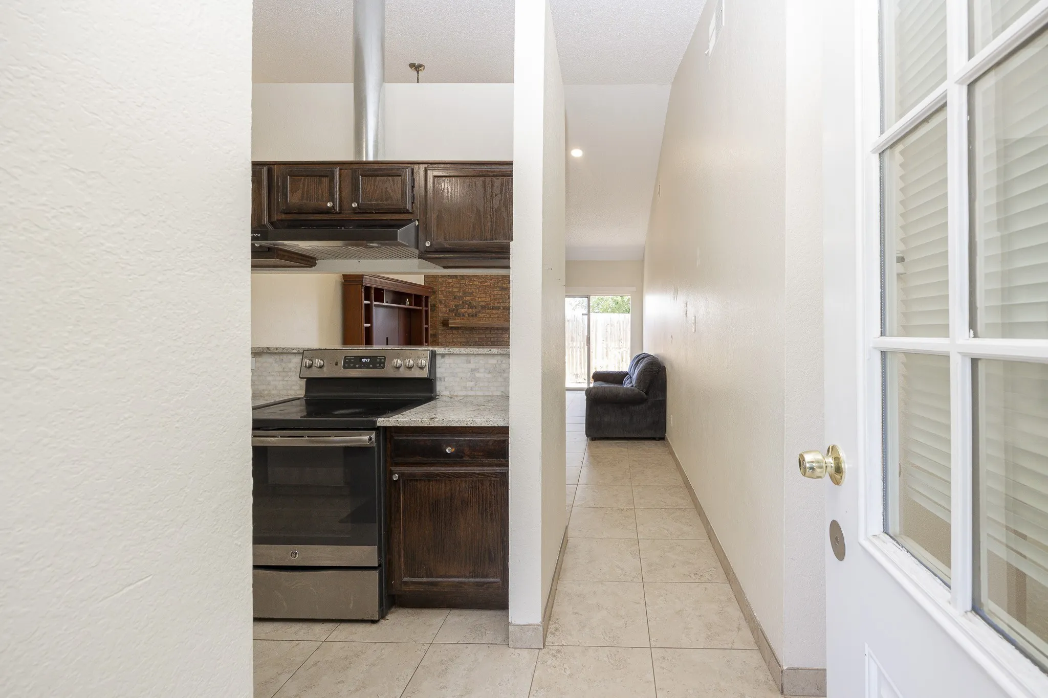 Stainless steel range and hood, granite-look countertops, tiled backsplash, wood-finish cabinetry, and tiled flooring