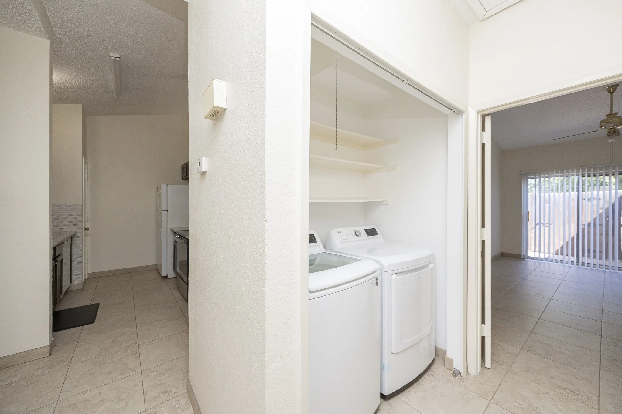 Tile flooring throughout, full-size washer and dryer, built-in shelving, sliding glass door, and a ceiling fan