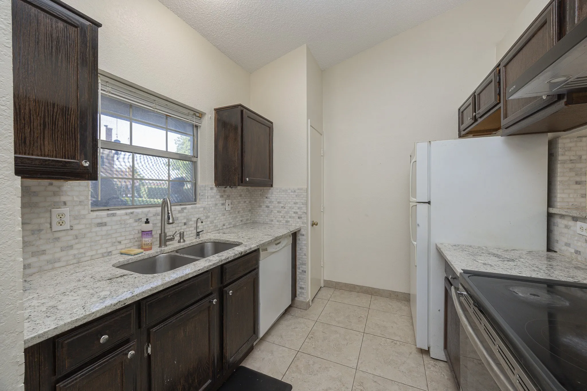 Kitchen featuring dark wood-finish cabinetry, light-toned countertops, and a full tile backsplash