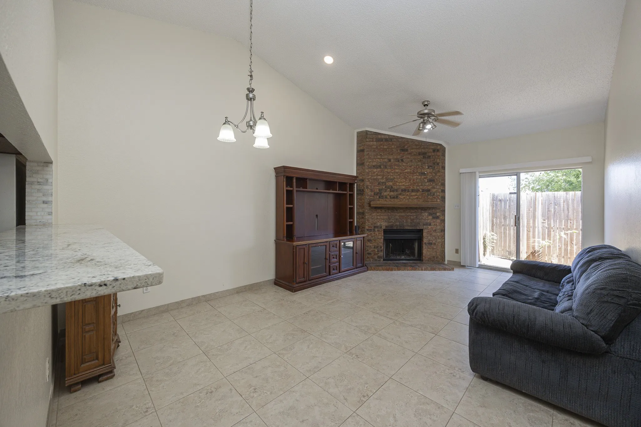 V-groove vaulted ceiling with a ceiling fan, brick-faced fireplace with a wood mantle, tile flooring, and a sliding glass door