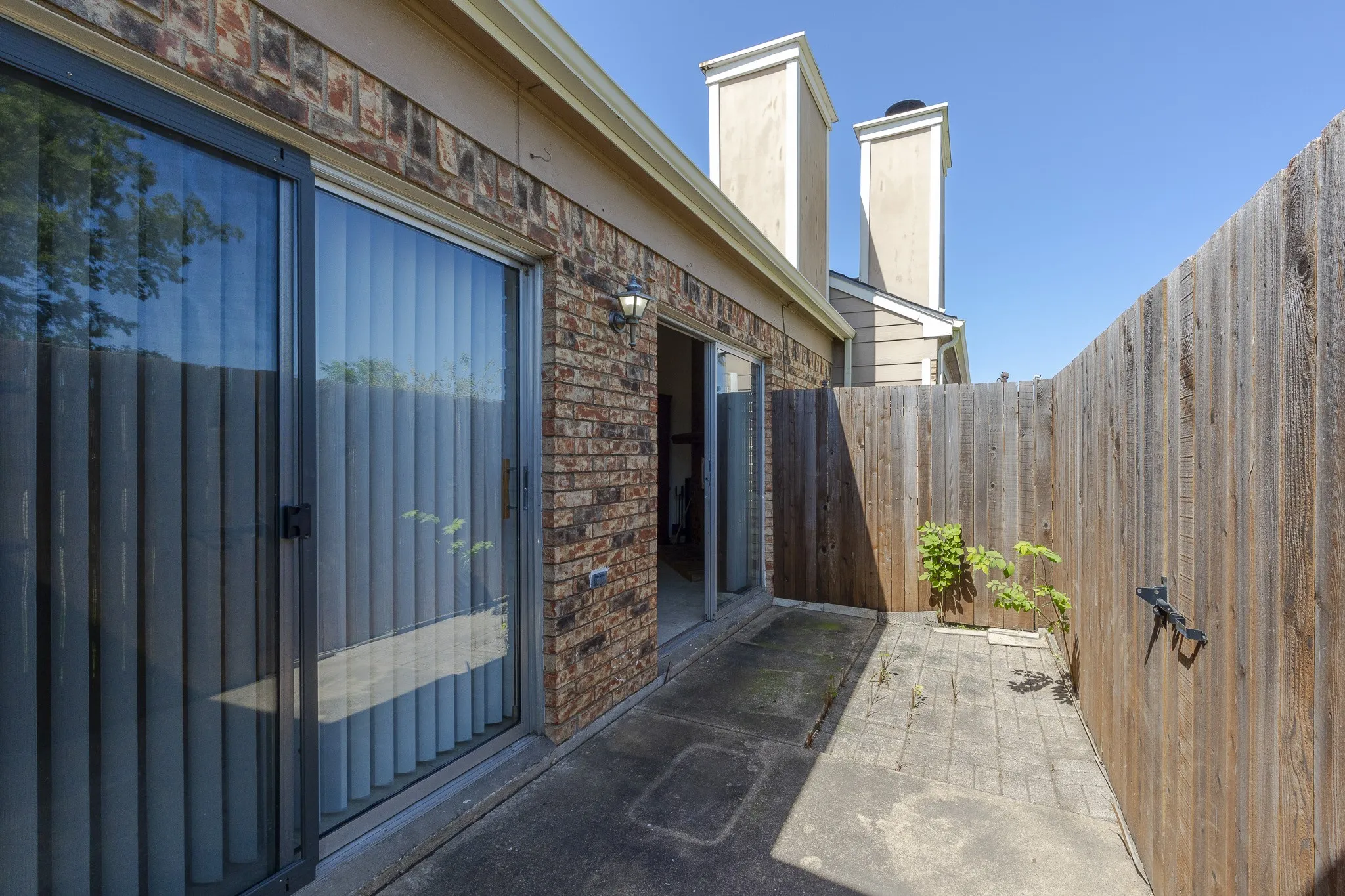 Private fenced patio featuring a paver stone surface, brick exterior, and dual sliding glass doors