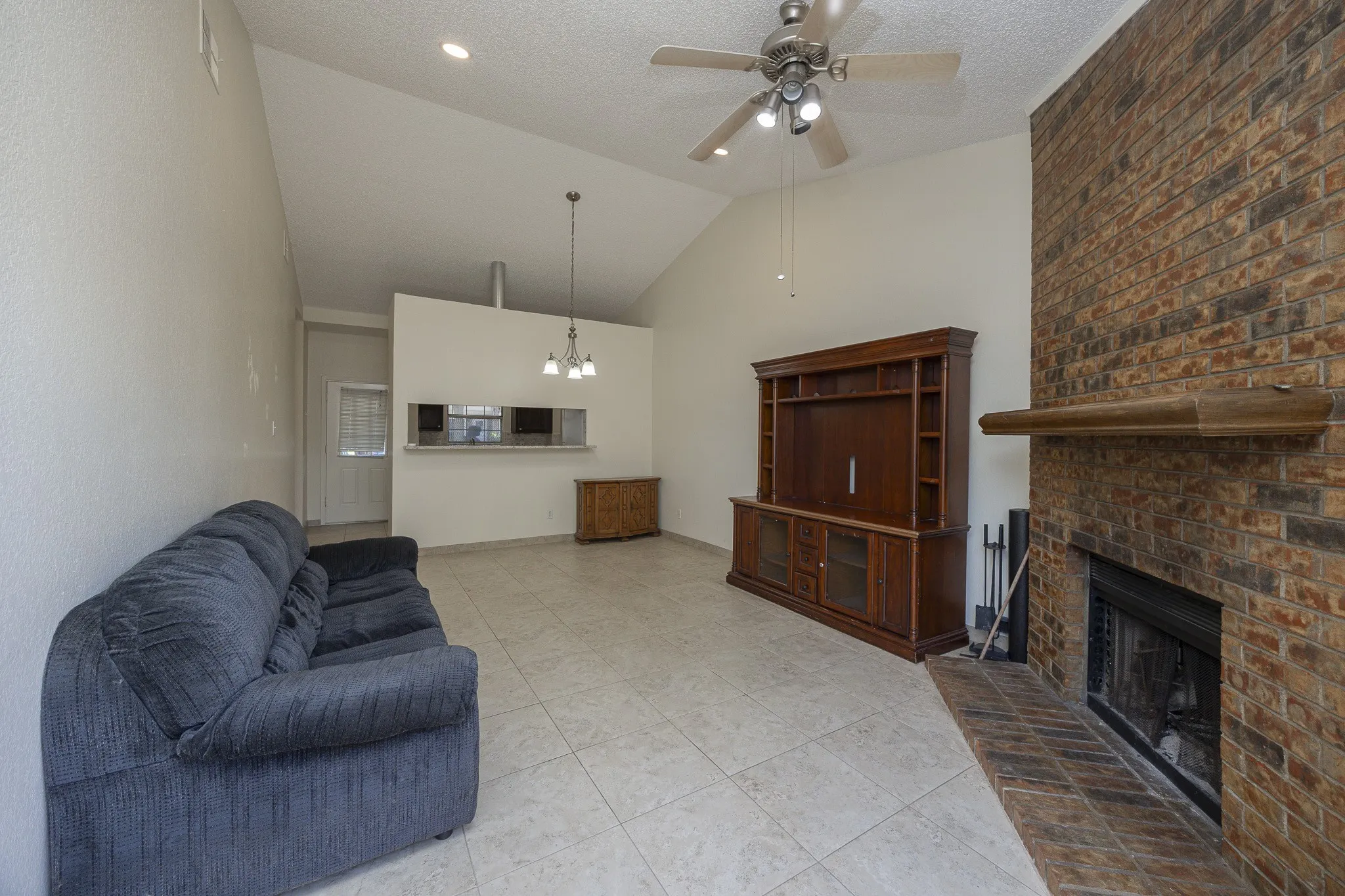 Vaulted ceiling with recessed lighting, ceiling fan, brick fireplace, and tile flooring