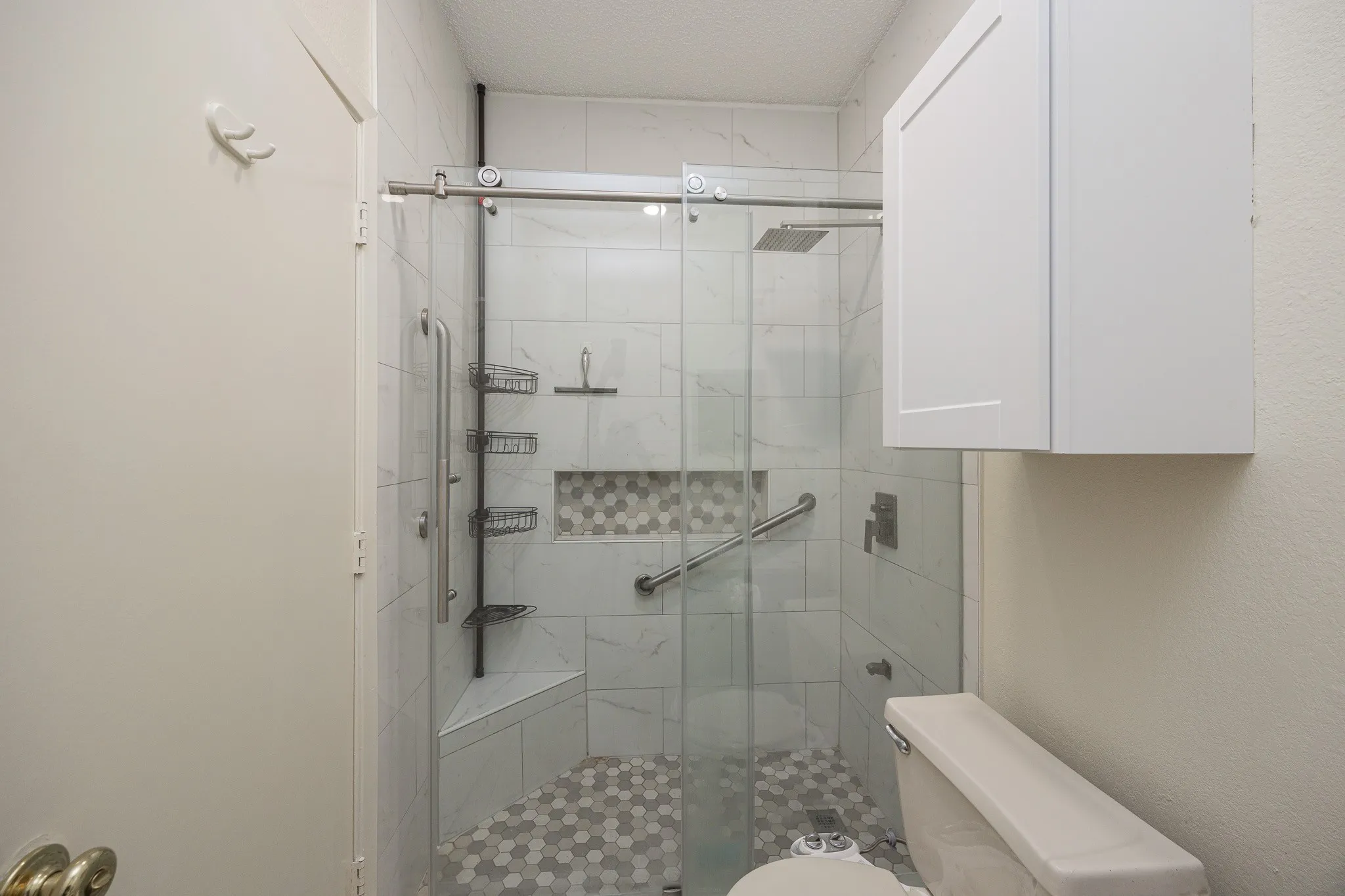 Glass-enclosed shower with a hexagon tile floor, a built-in bench, and a recessed tiled niche