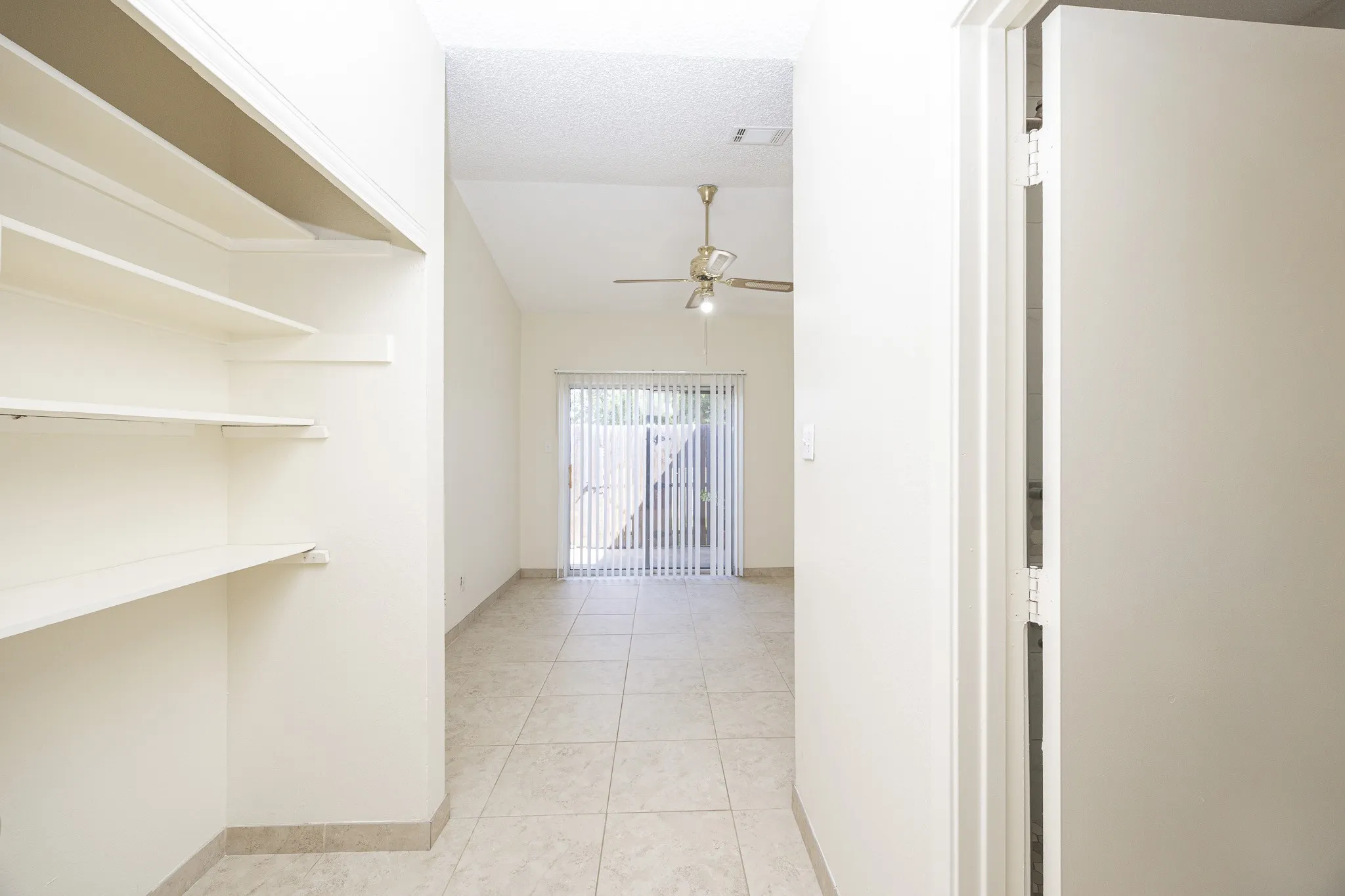 Built-in shelving, vaulted ceiling, tile flooring, ceiling fan with light fixture, and sliding glass door