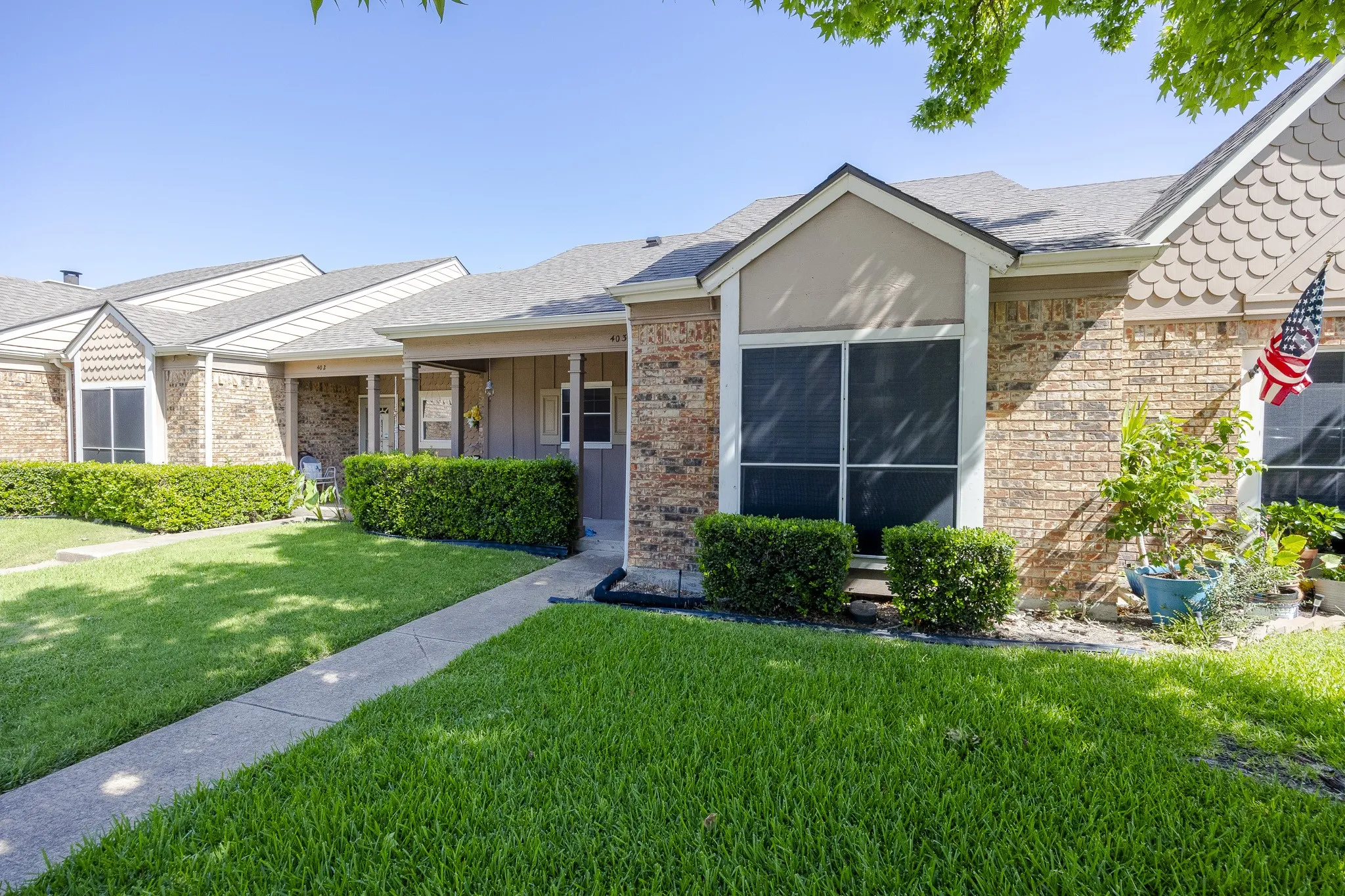 Brick exterior facade with gabled roofline, front shrubbery, and a concrete walkway