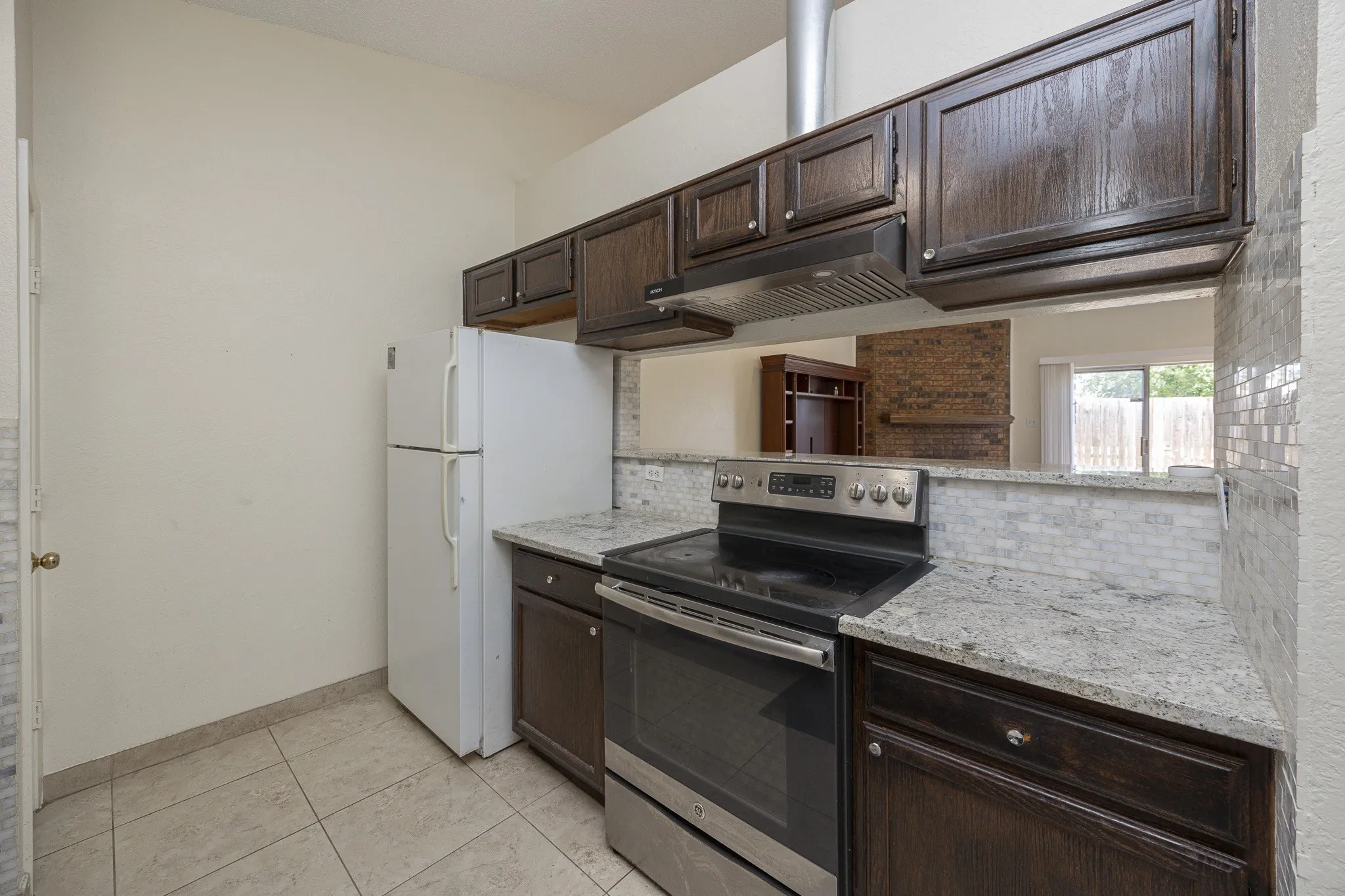 Kitchen featuring wood cabinets, light-toned stone countertops, stainless steel range, and a mosaic tile backsplash
