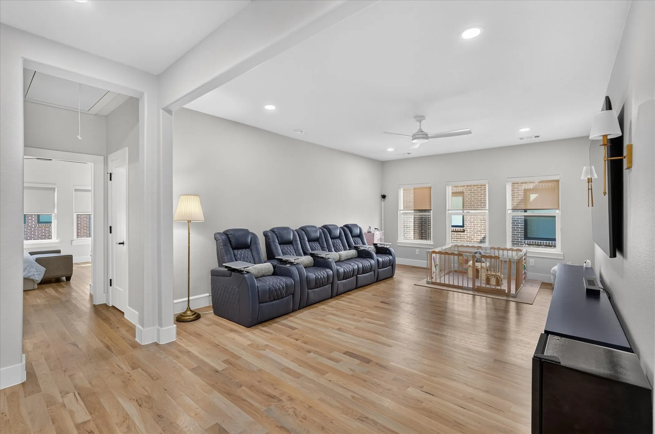 Spacious room featuring wood-finish flooring, recessed lighting, a ceiling fan, and multiple windows with roller blinds