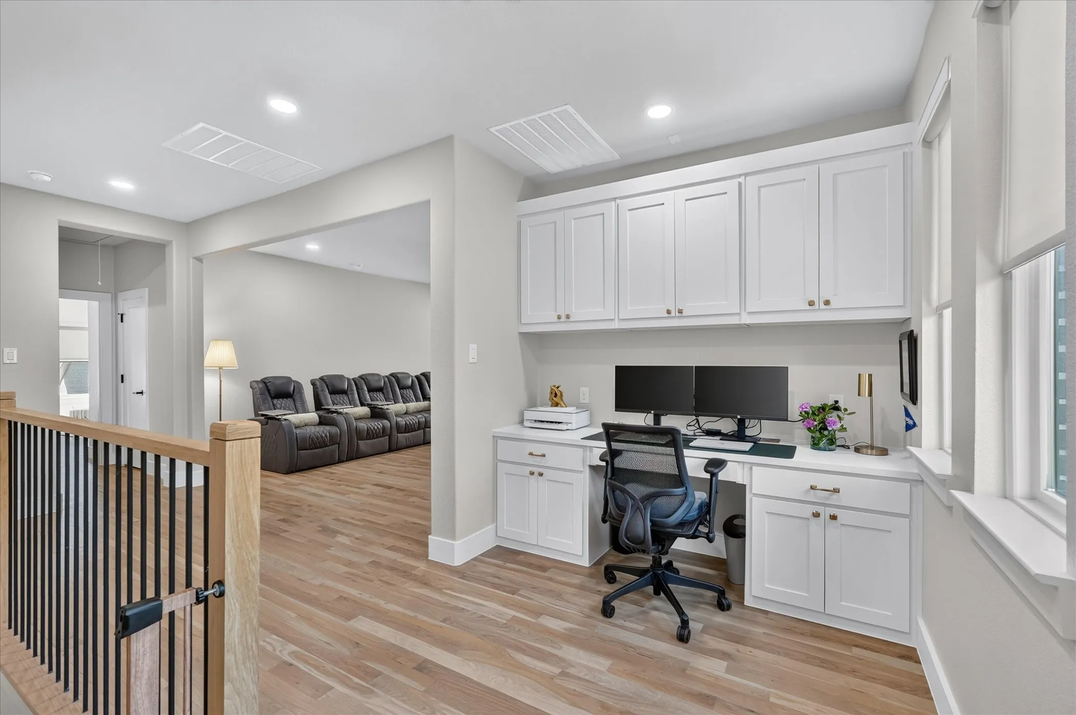 Hardwood flooring, custom built-in desk, white shaker cabinetry, recessed lighting, and a modern stair railing