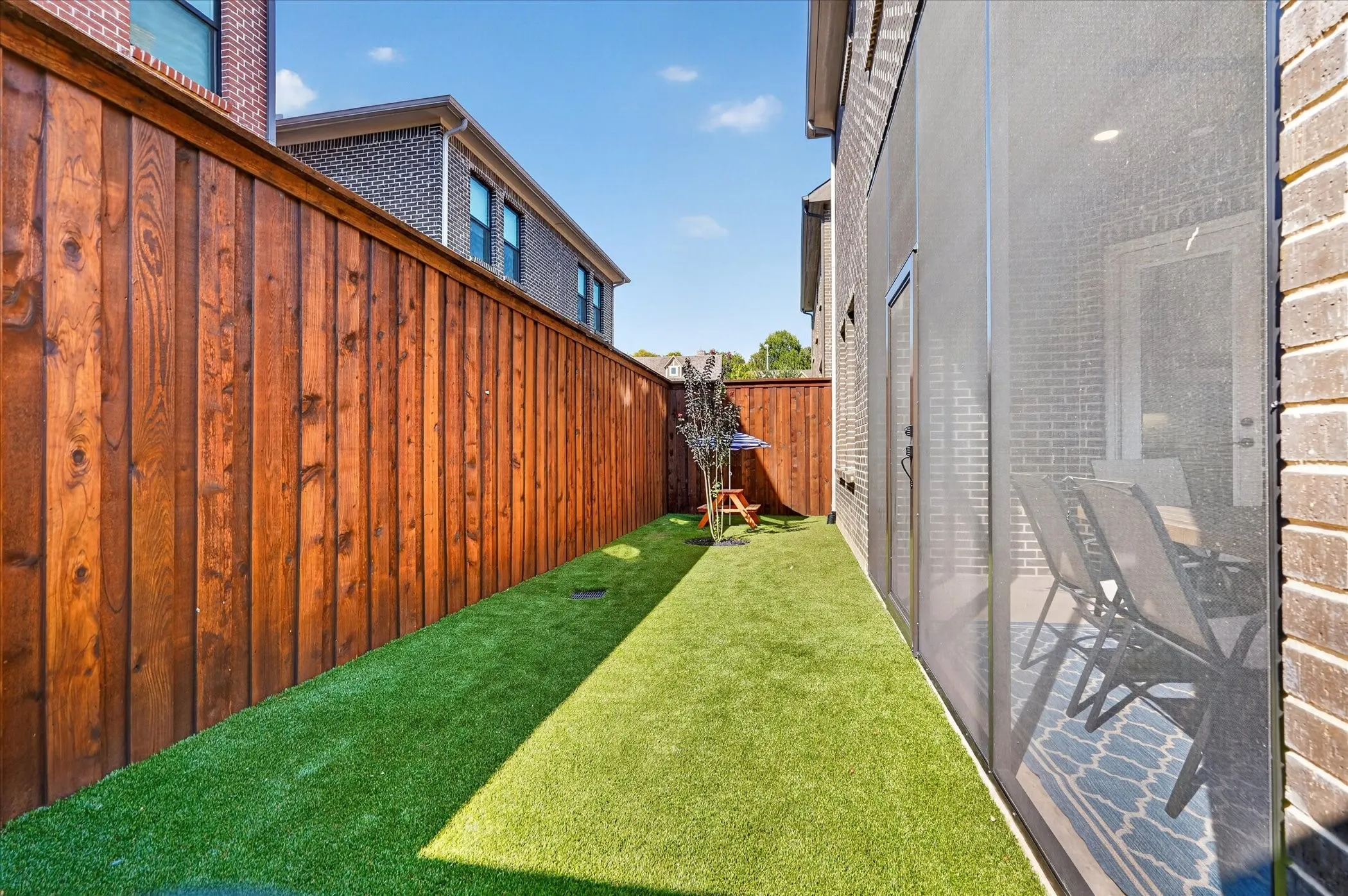 Fenced outdoor area with artificial turf, brick exterior, and a screened patio