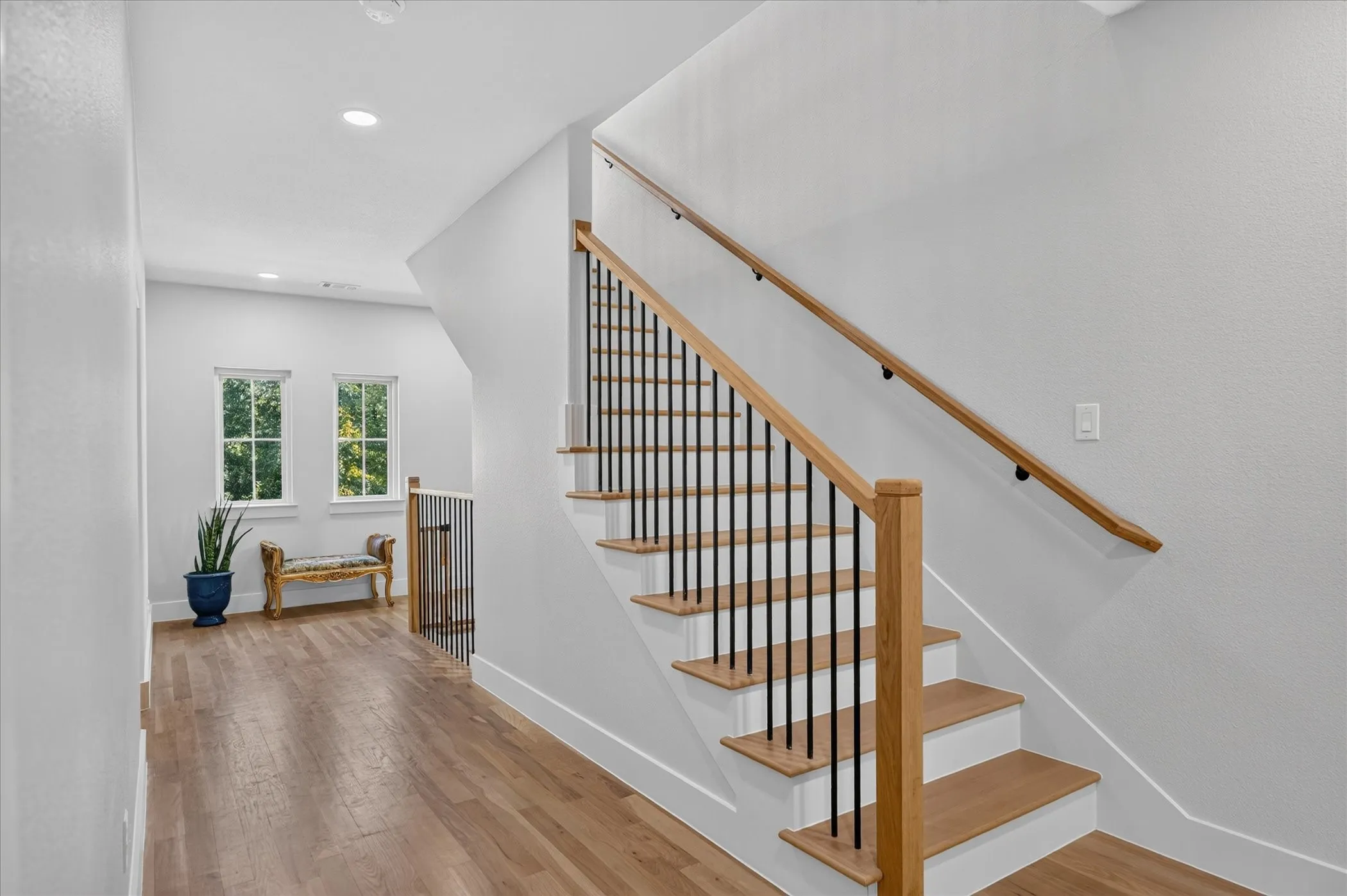 Wood-finish flooring throughout, white walls, recessed ceiling lighting, and a staircase with wood treads, black balusters, and wood handrails